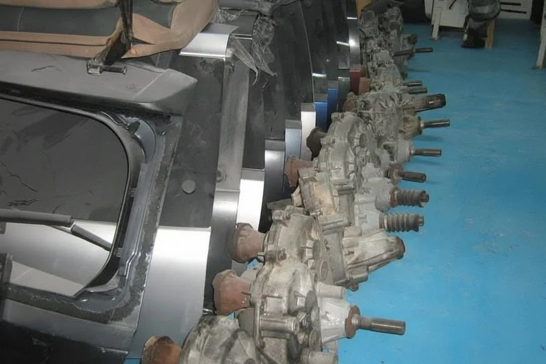 A line of four automotive transmission or engine components placed on a metallic workbench in a workshop with a blue floor.