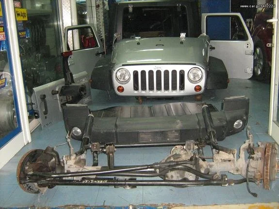 Disassembled Jeep vehicle with the front panel and internal components removed, and the body placed upright behind the frame, in a workshop setting.