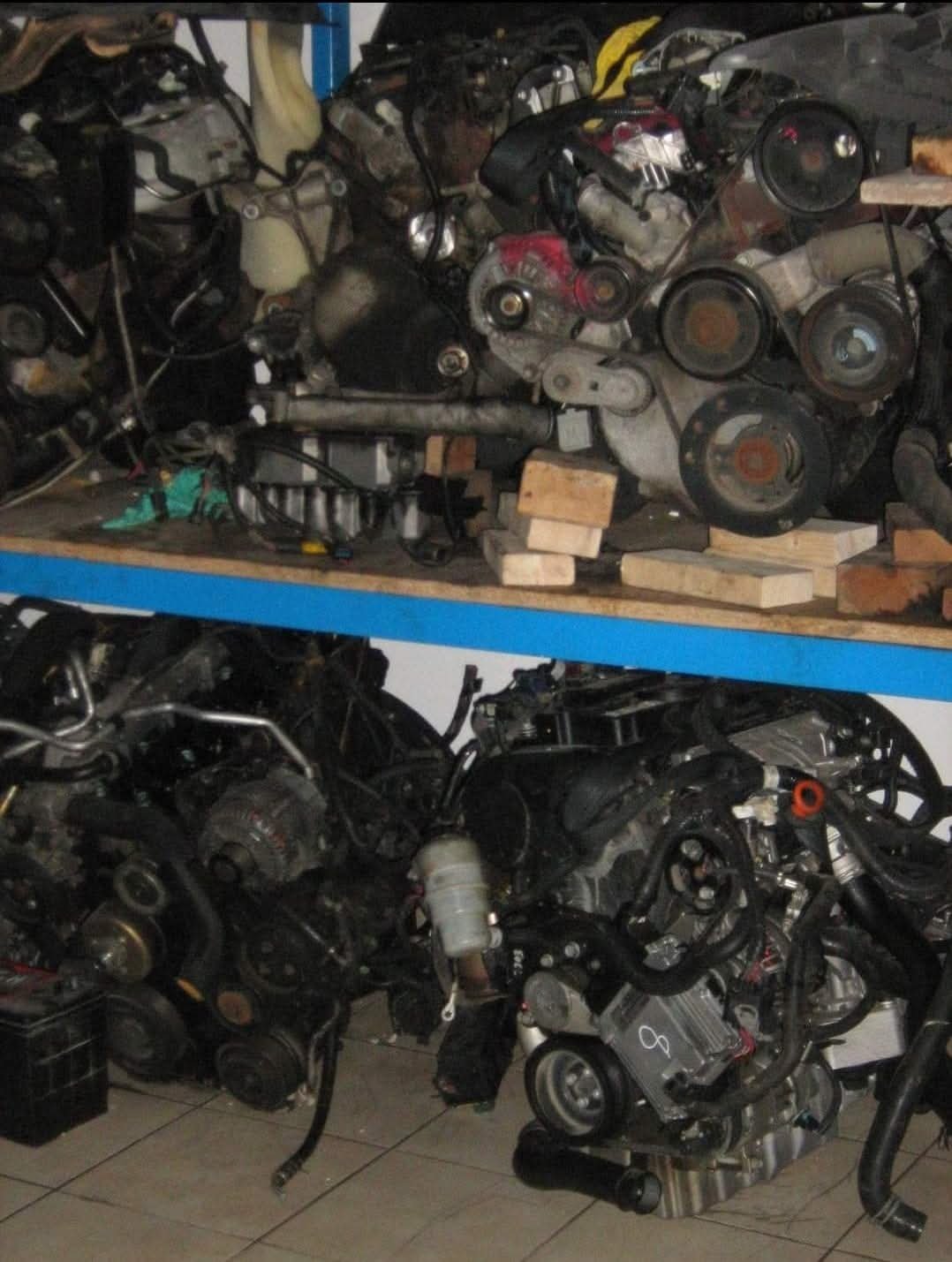 Suspended motorcycle engines on a blue shelf, with various engine parts and components in a workshop or storage area.