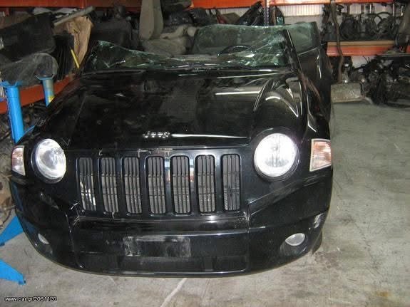 Black Jeep parked inside a garage or warehouse with automotive parts and equipment around.