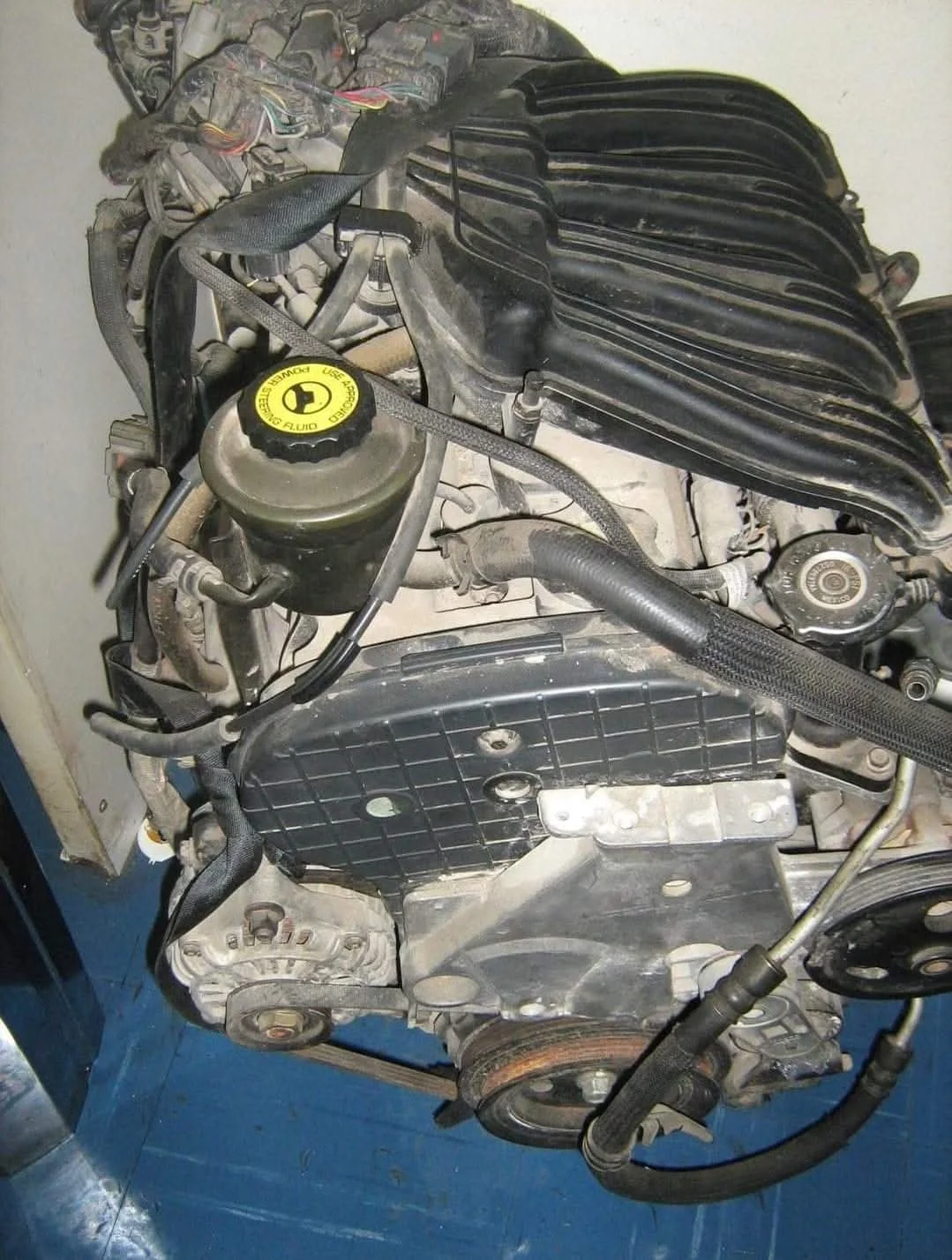 Automobile engine with various components including a yellow oil cap, black intake manifold, and serpentine belt.