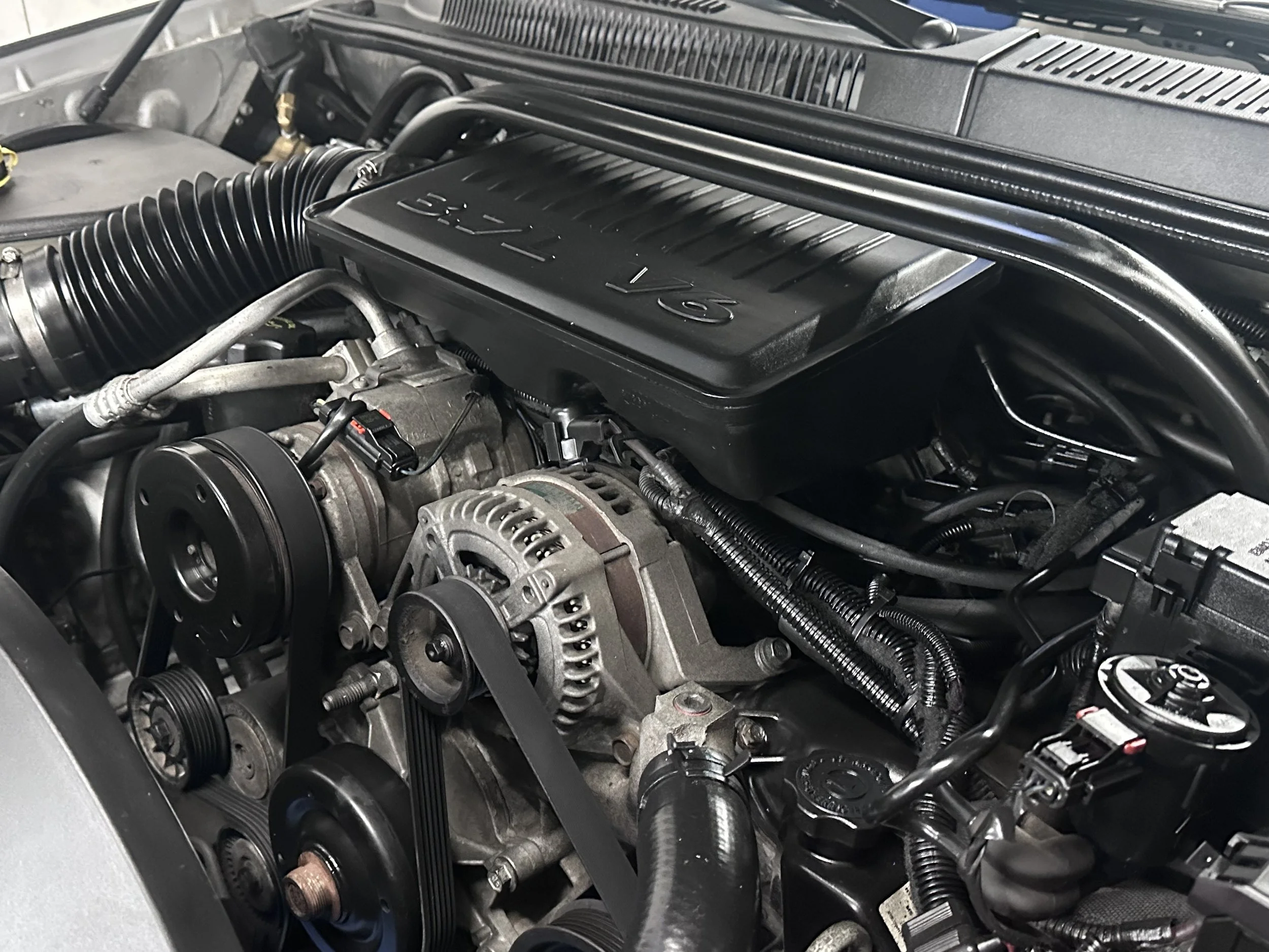 Close-up of a car engine showing belts, pulleys, alternator, and various components under the hood.