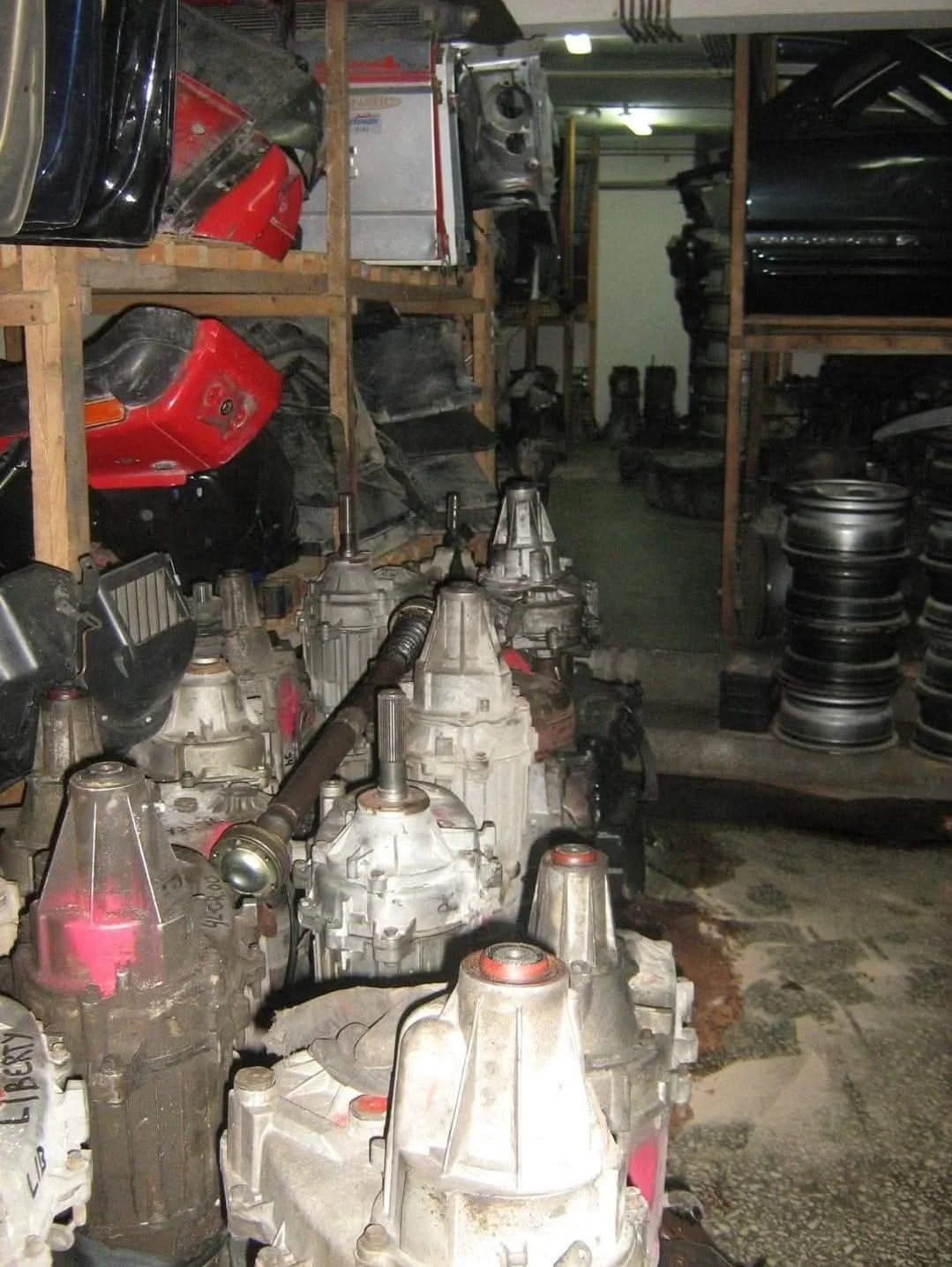 Shelves filled with car parts including transmissions, wheels, and bumpers in a workshop or storage area.