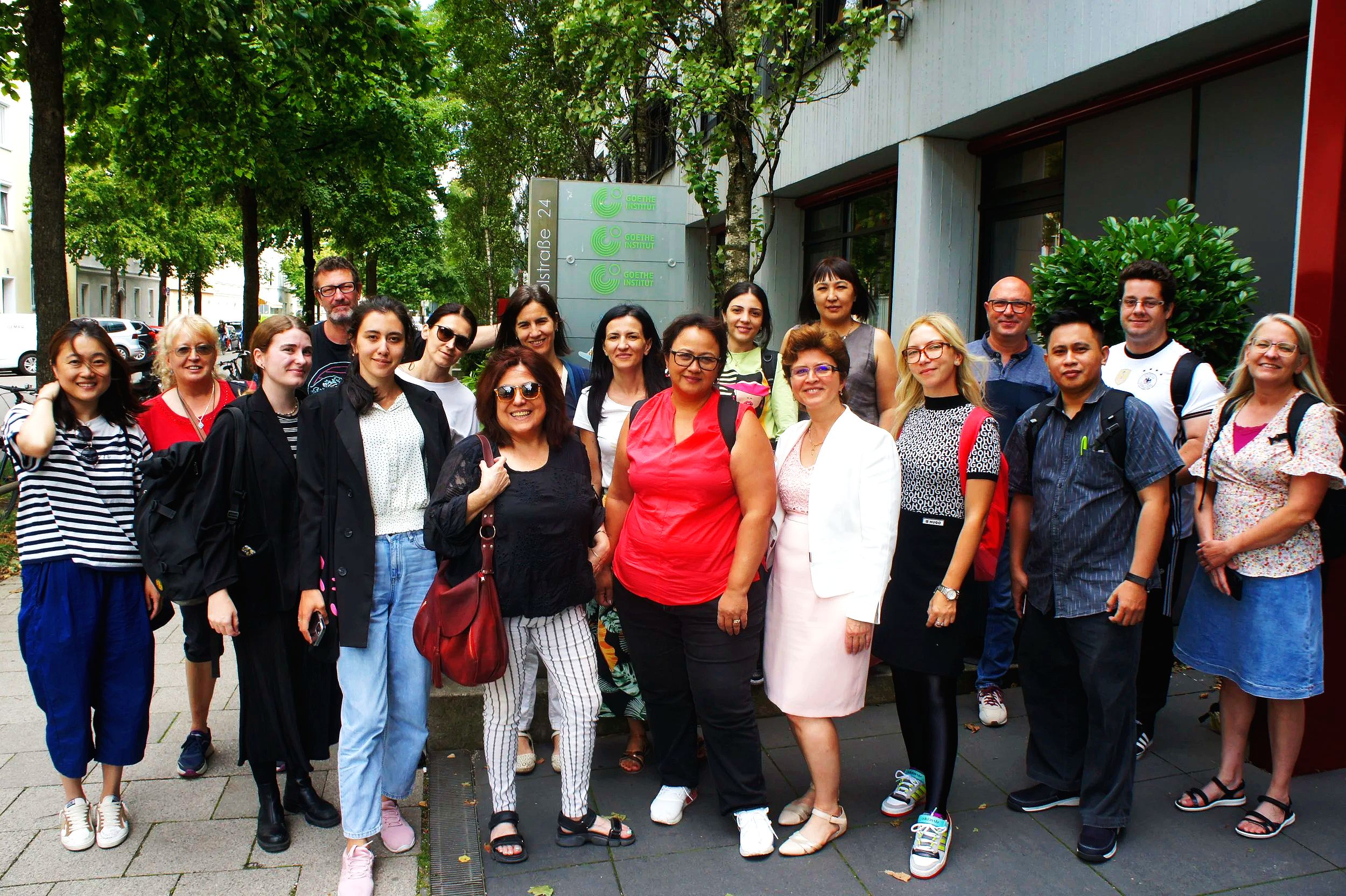 A group of diverse people standing on a sidewalk outdoors, smiling for a photo.