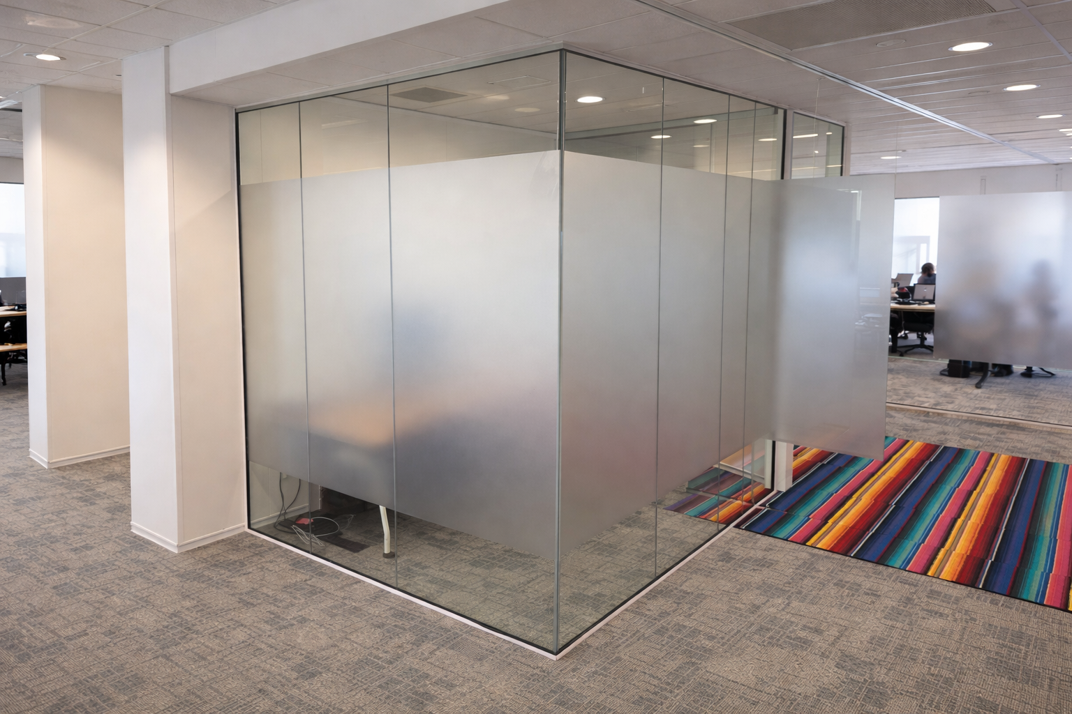 Kantoorruimte met glazen scheidingswanden en een kleurrijk tapijt.