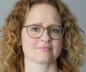 Nahaufnahme eines Frauengesichts mit lockigem, rotem Haar und Brille