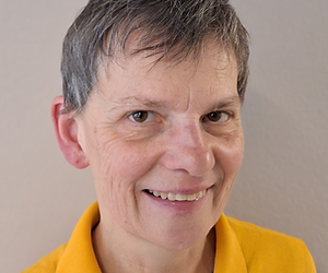 Nahaufnahme eines lächelnden Mannes mit kurzen grauen Haaren, trägt ein gelbes Polohemd, vor neutralem Hintergrund.