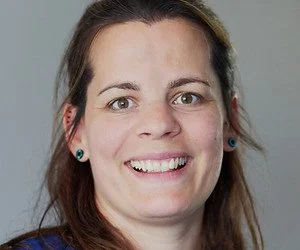 Nahaufnahme eines lächelnden Frauengesichts mit braunen Haaren, blauen Augen und blauer Kleidung