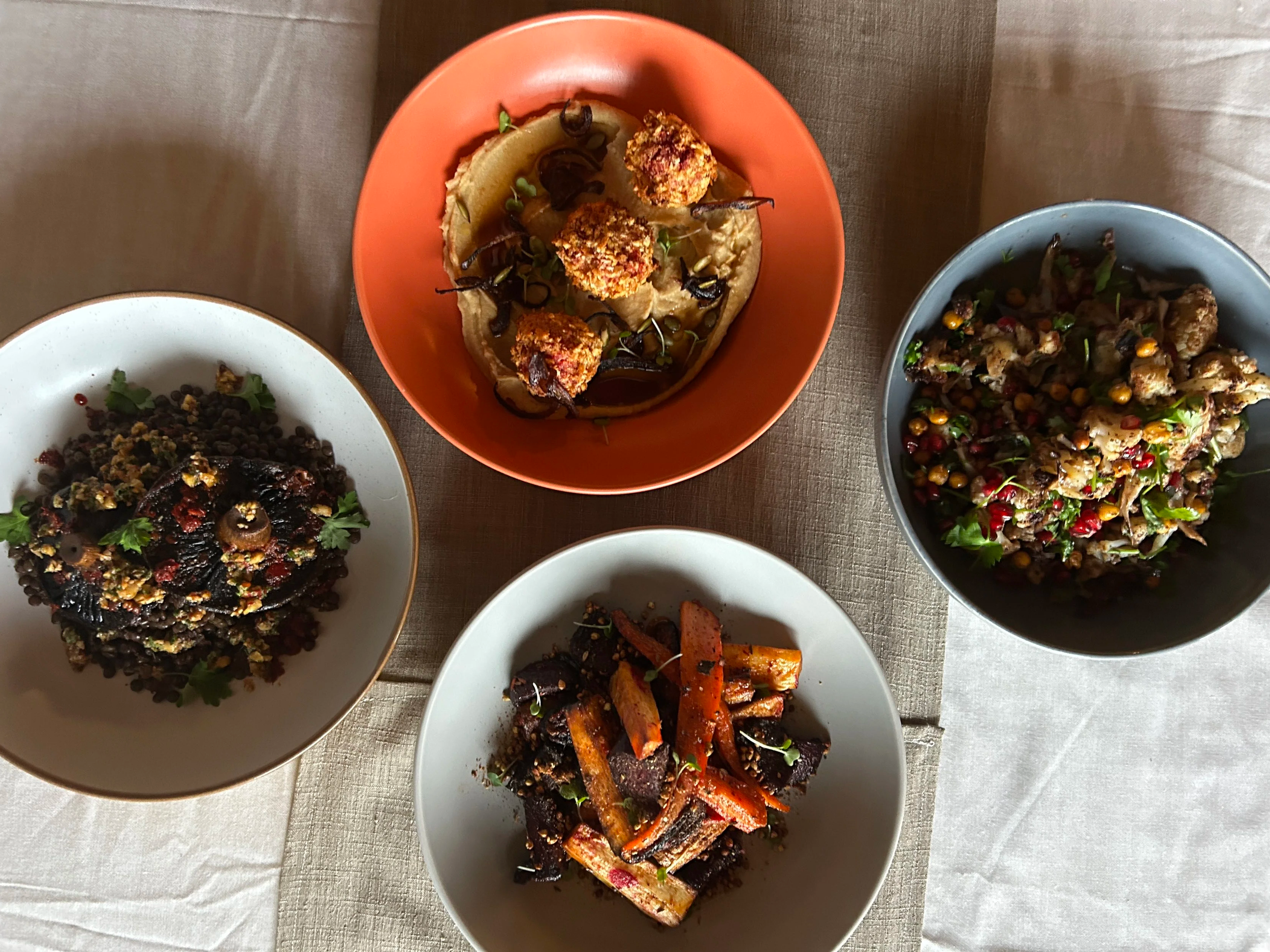 An overhead view of five plates with various Ethiopian dishes, including lentil stew, vegetable mix, salad, and injera bread.