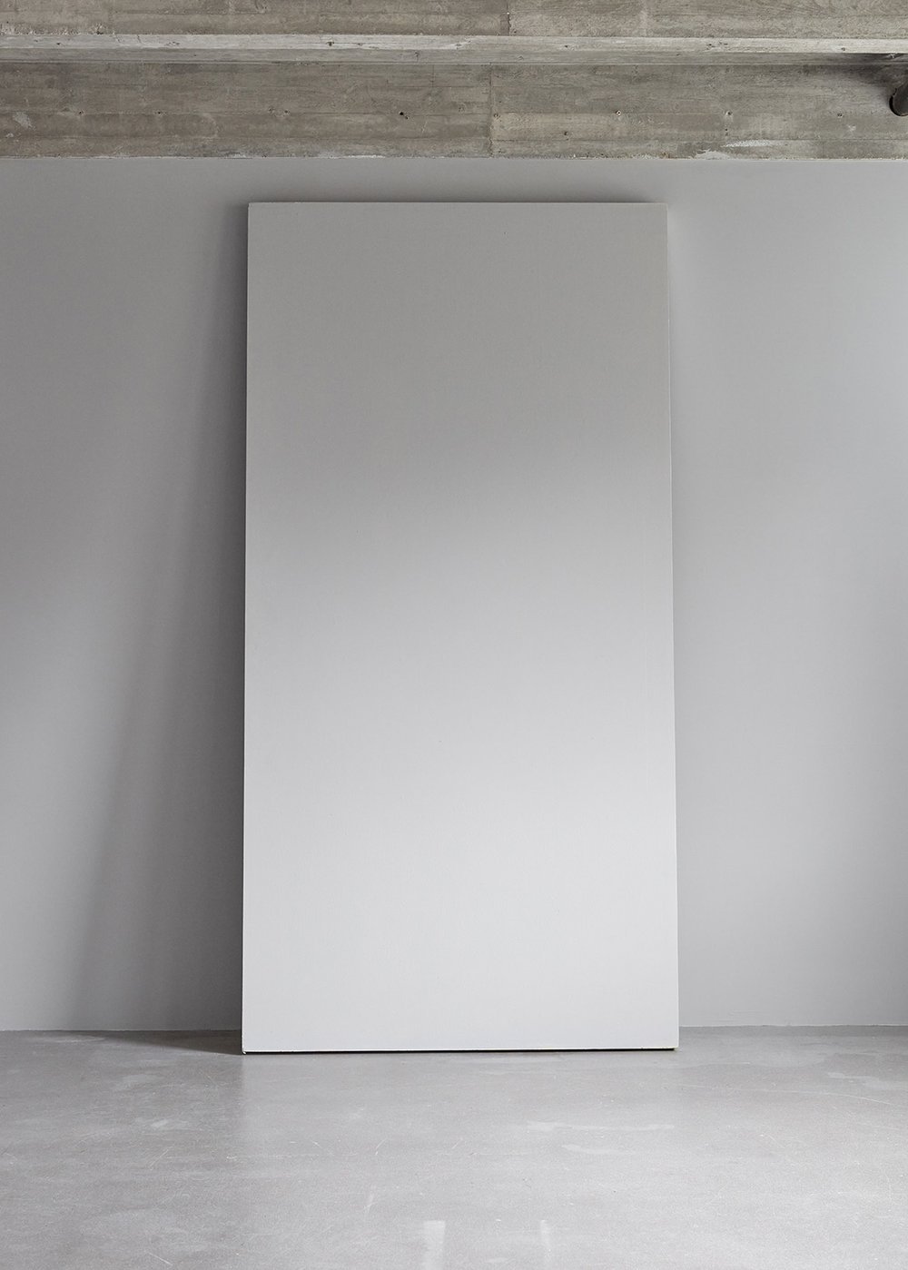 A large blank white rectangular canvas leaning against an unfinished concrete wall in a minimalistic room.
