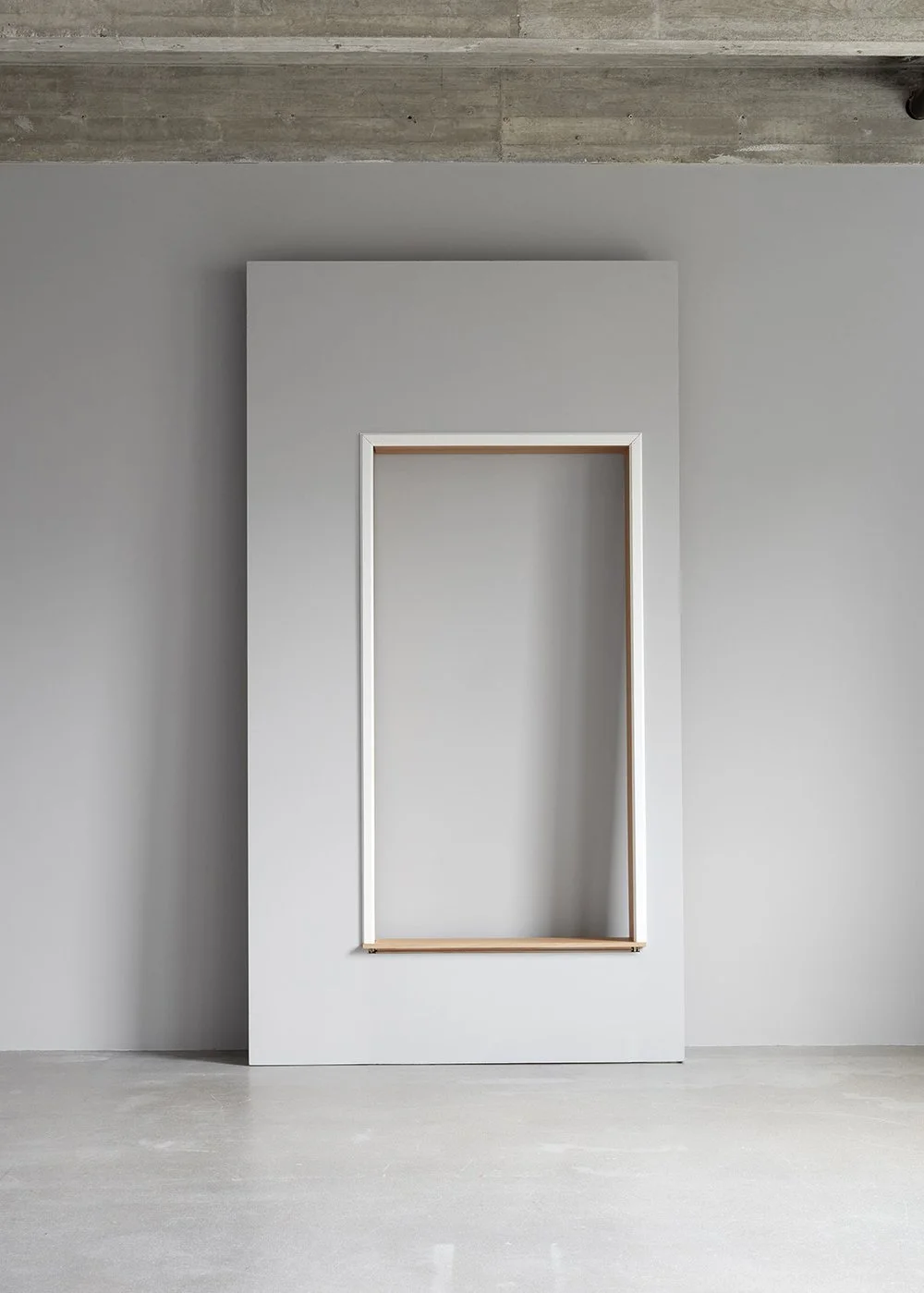 Minimalist interior with a white wall, a large rectangular empty picture frame, and a grey ceiling with visible concrete texture.