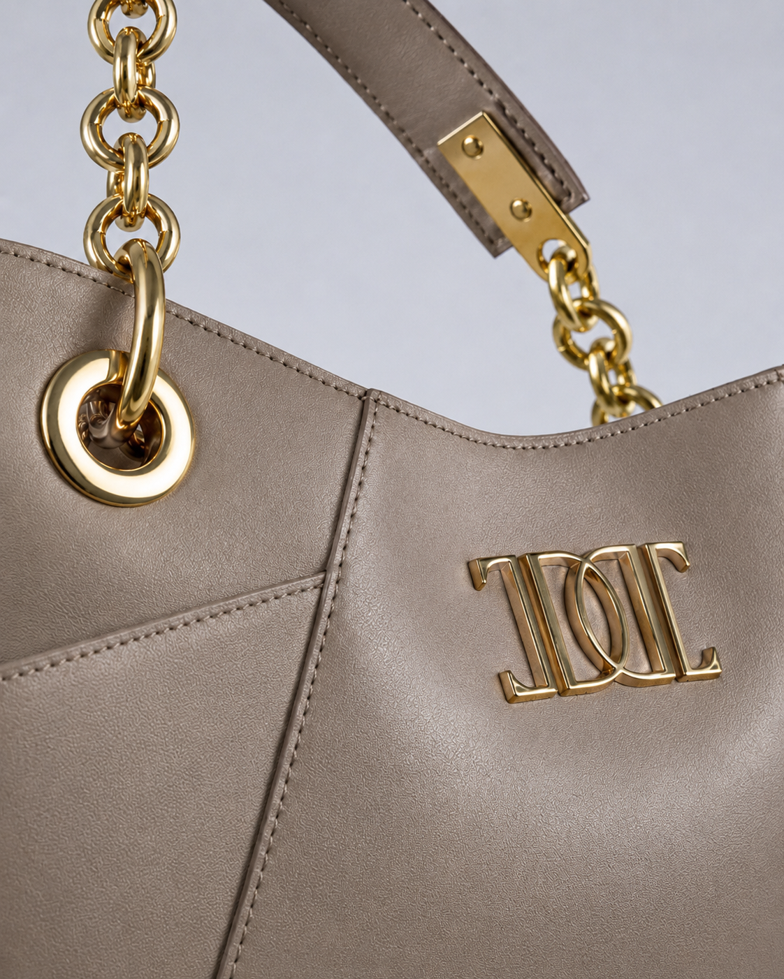 Close-up of a beige leather tote bag with gold chain handles and a gold logo.