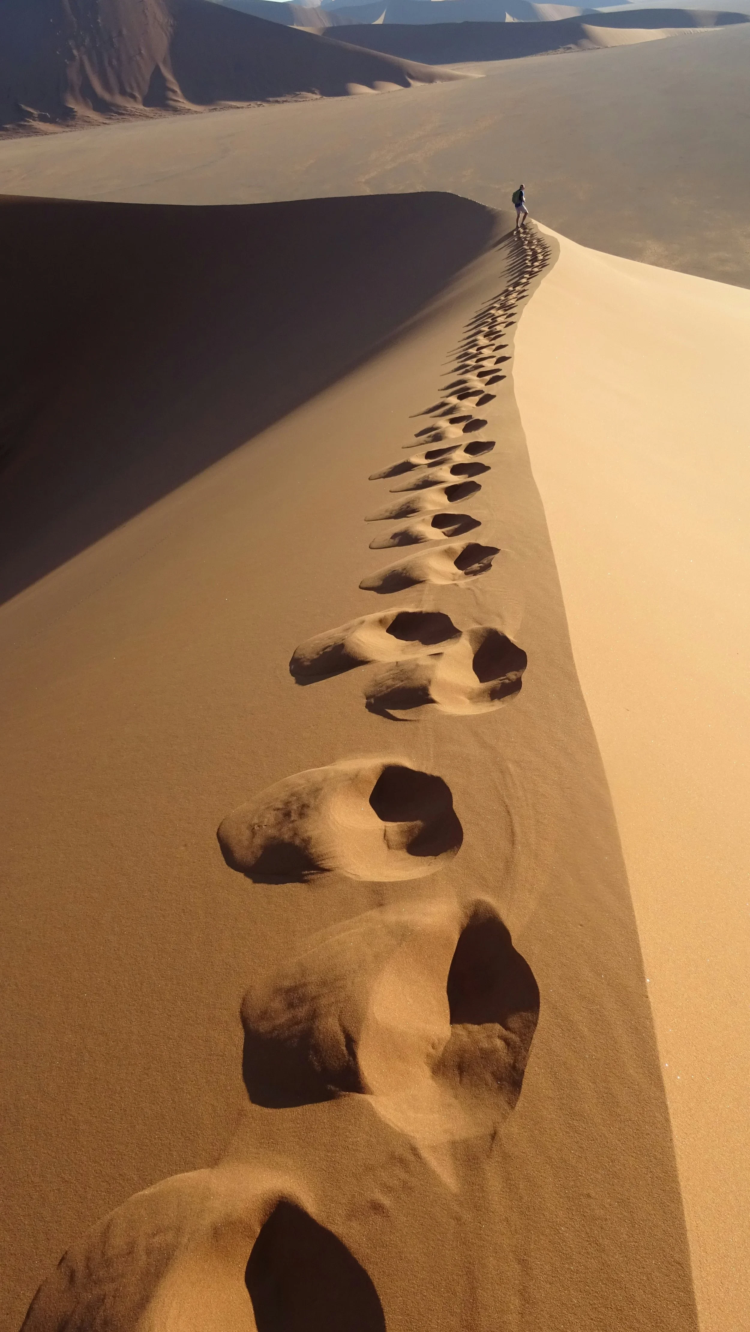 A man walking across the desert dunes, leaving footprints in the sand.