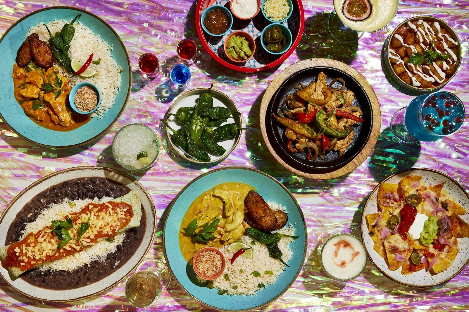 Assorted Mexican dishes on a colorful table, including rice and chicken, tacos, fajitas, and various sauces and drinks.