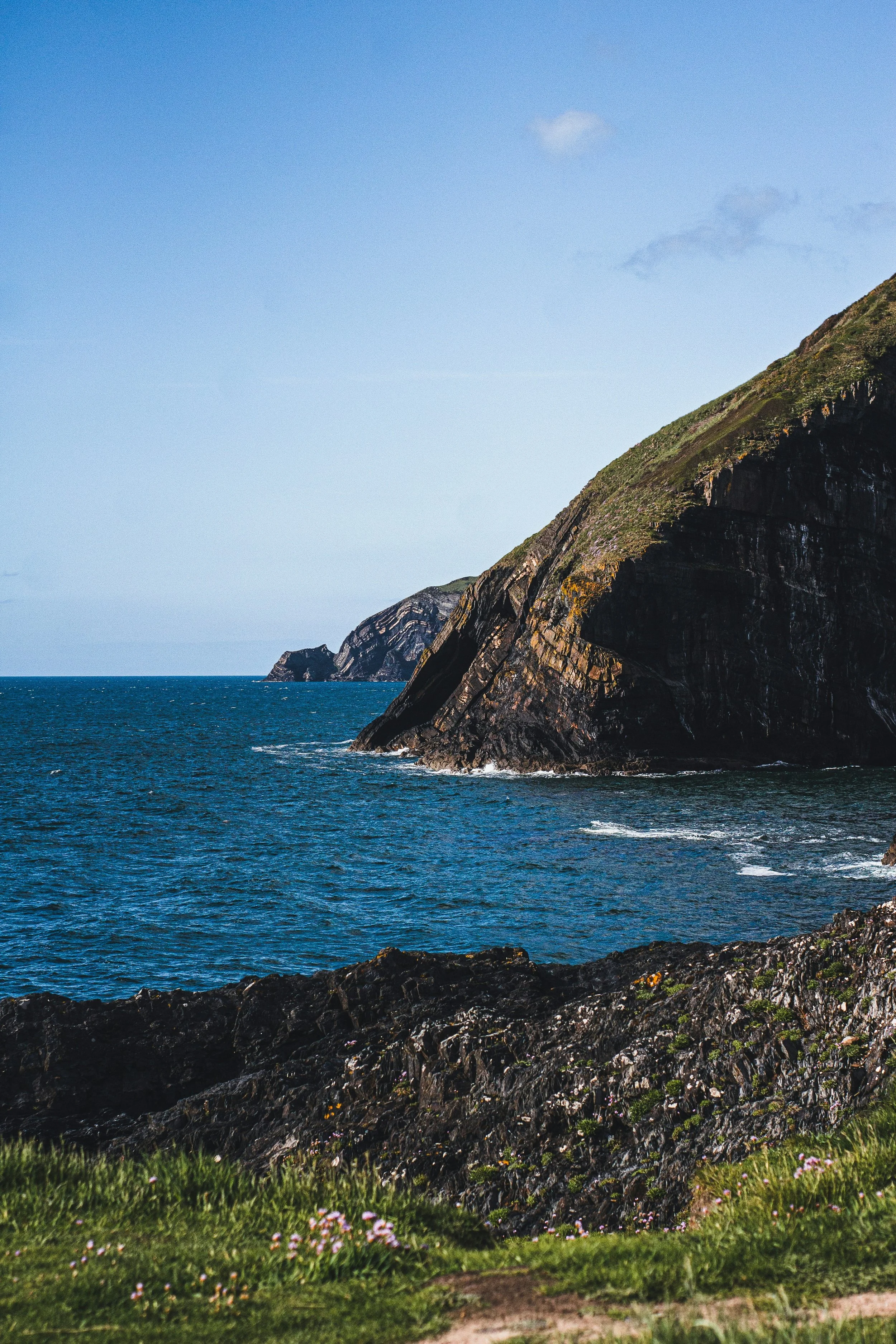 Coastal landscape with rocky cliffs and ocean under a clear blue sky.