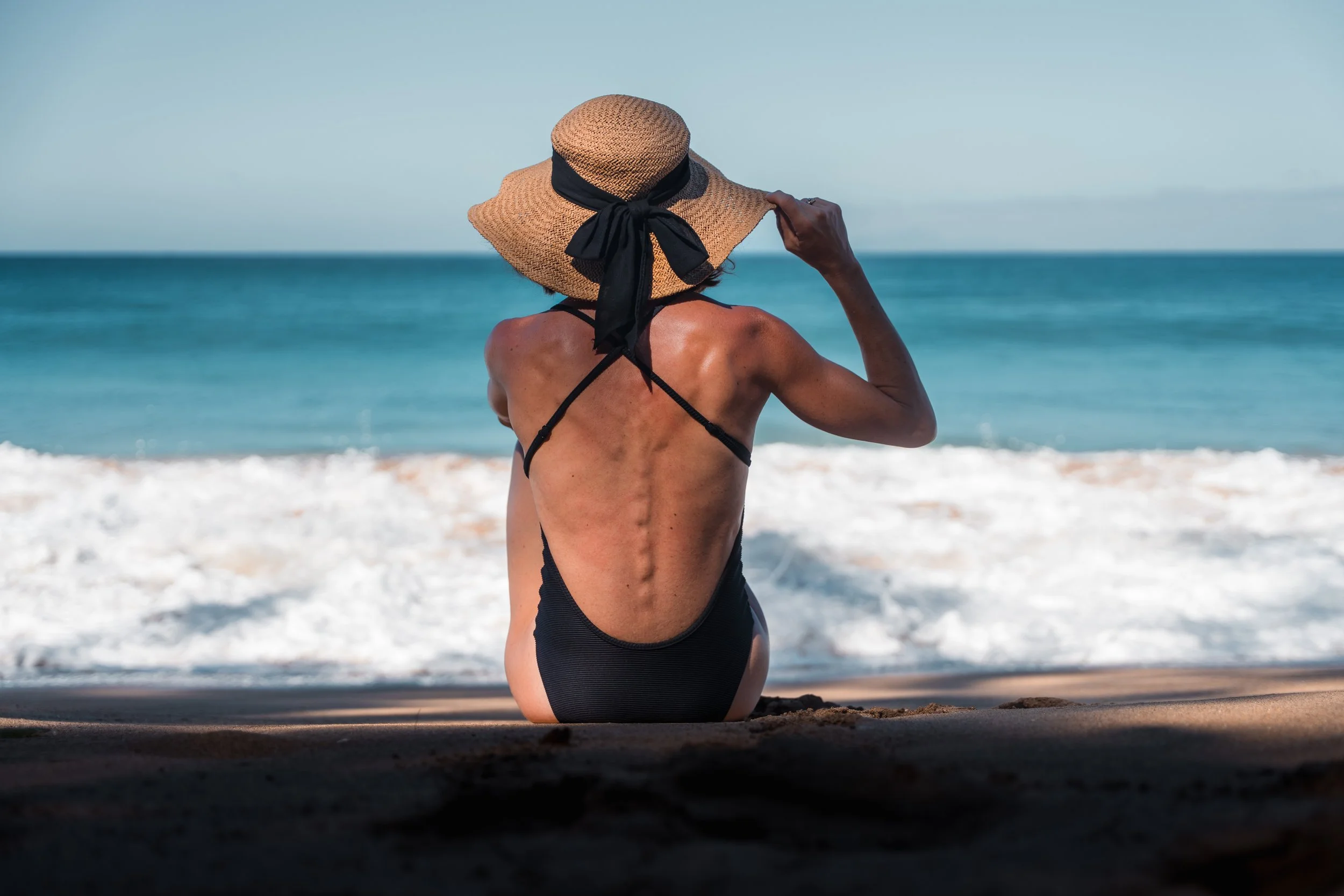 Femme au chapeau de dos regardant l’océan
