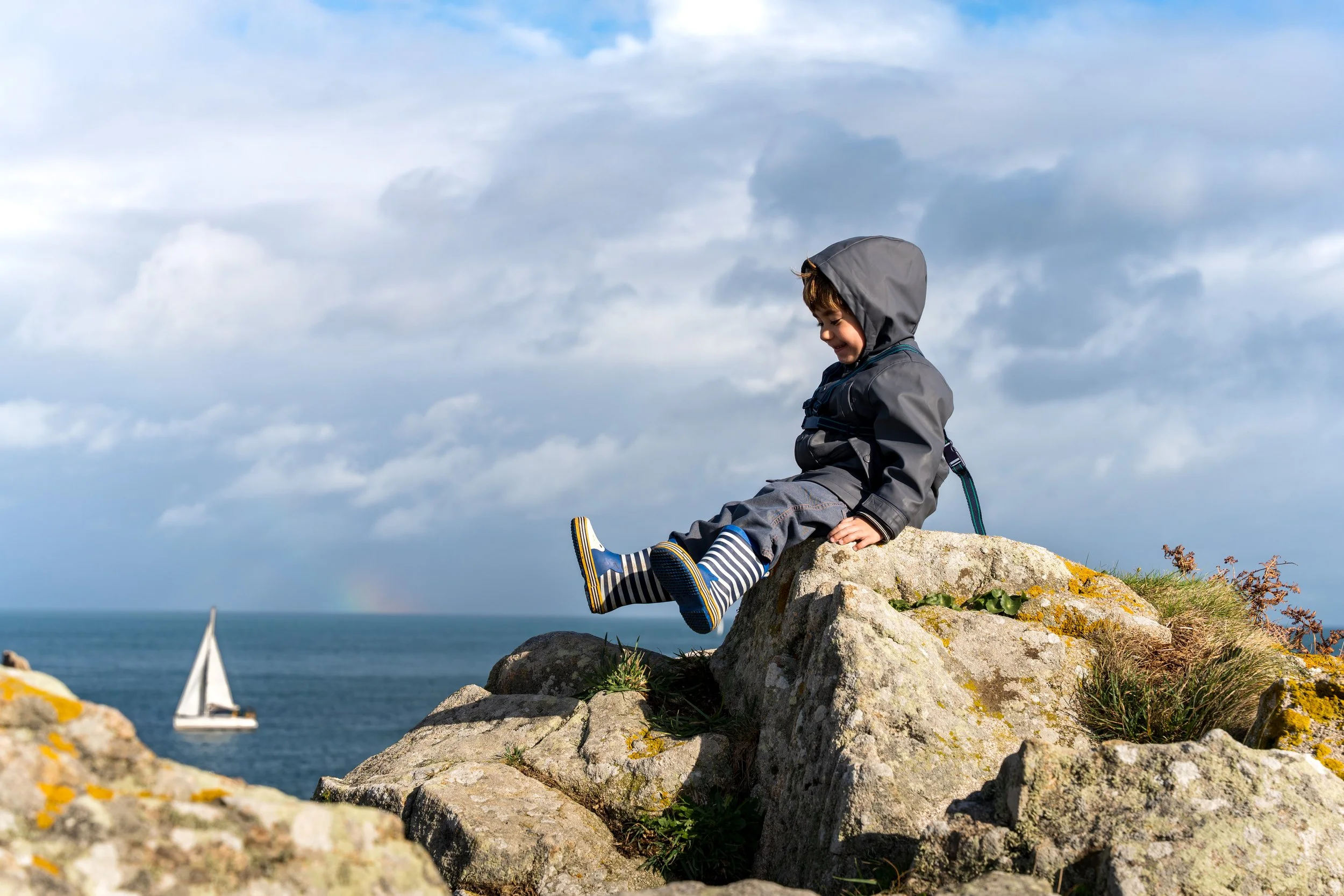 Enfant en tenue de pluie devant un panorama avec un bateau
