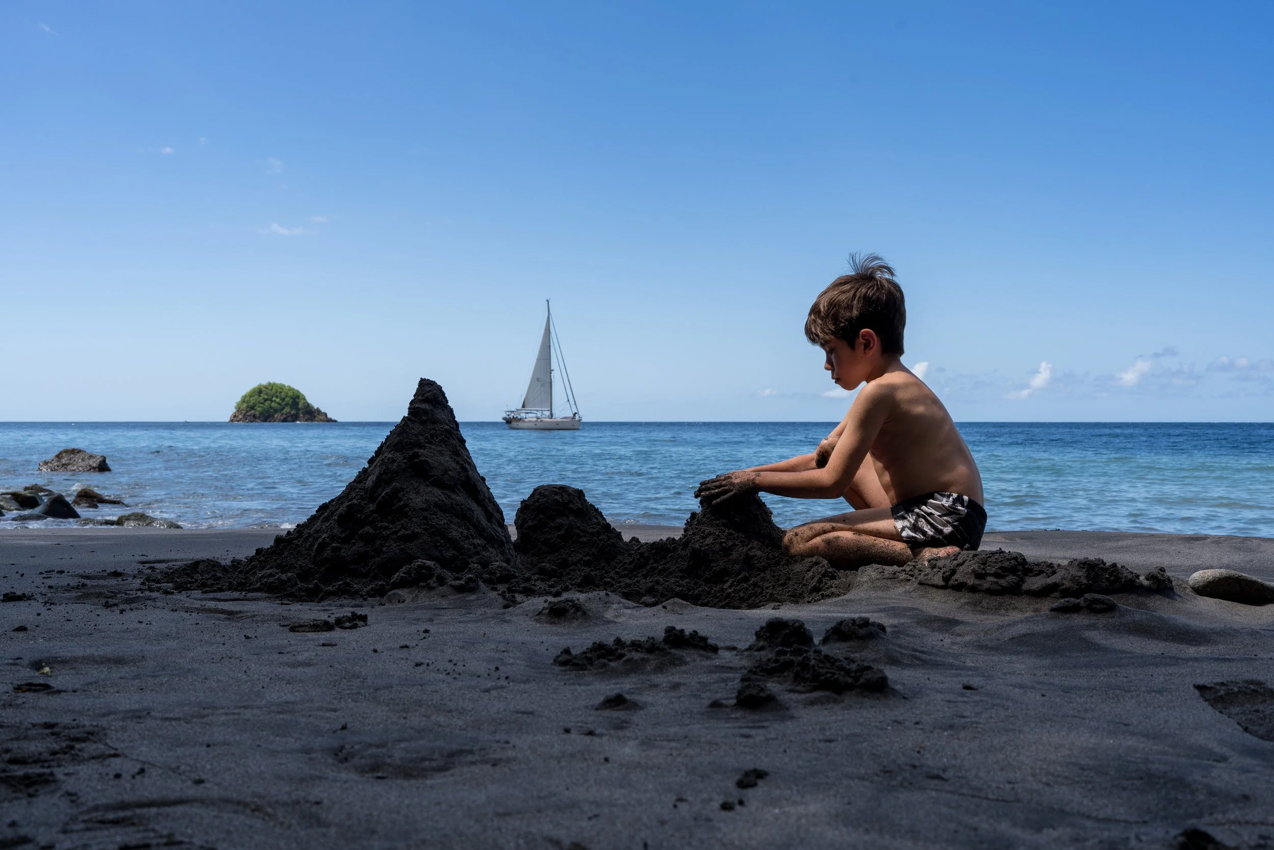 Enfant à la plage, petit bateau et château de sable