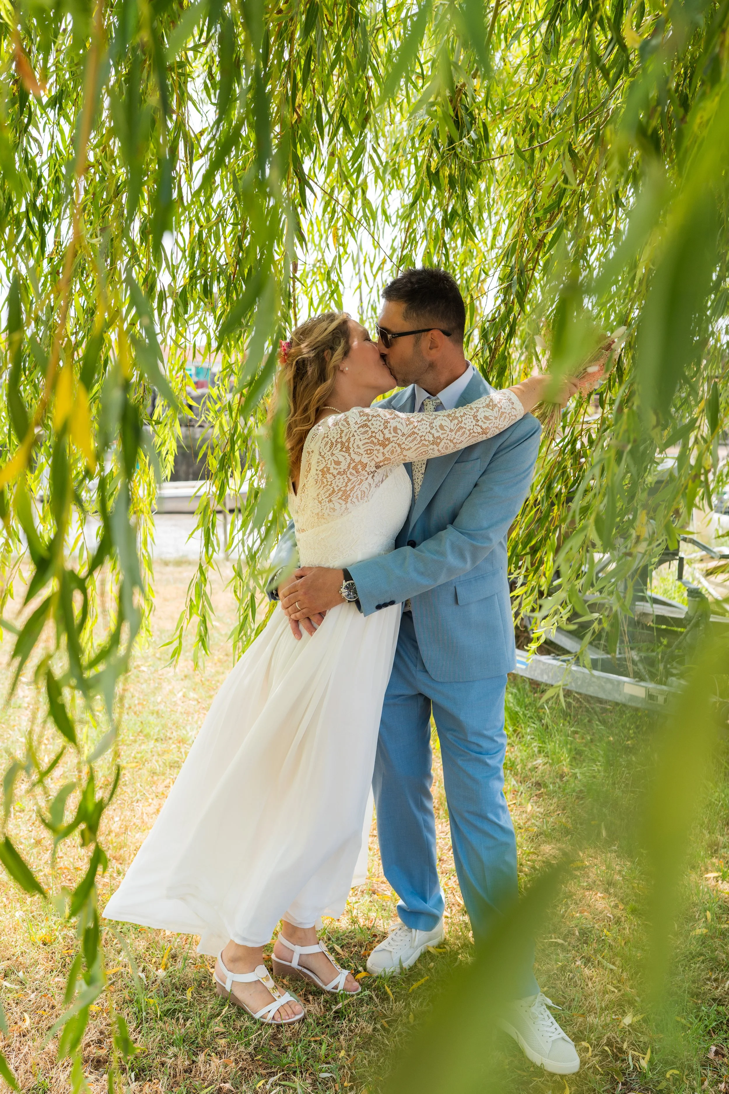 Les jeunes mariés s’embrassent à l’ombre d’un saule - mariage