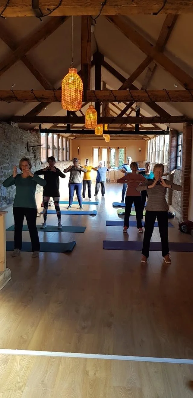 A group of people practicing yoga in a rustic studio with wooden beams and pendant lights.