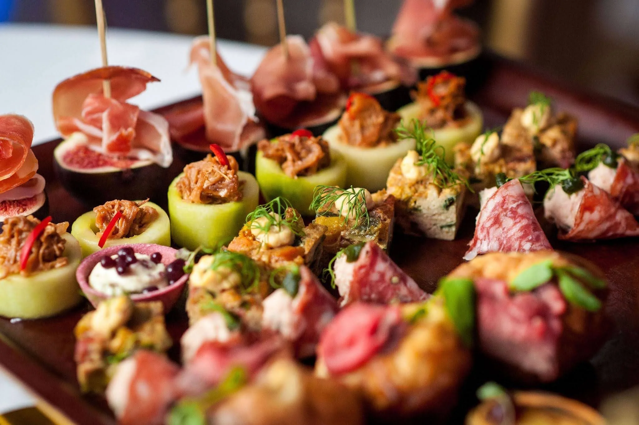 Assorted bite-sized appetizers, including stuffed vegetables, cured meats, and garnishes, arranged on a serving tray.