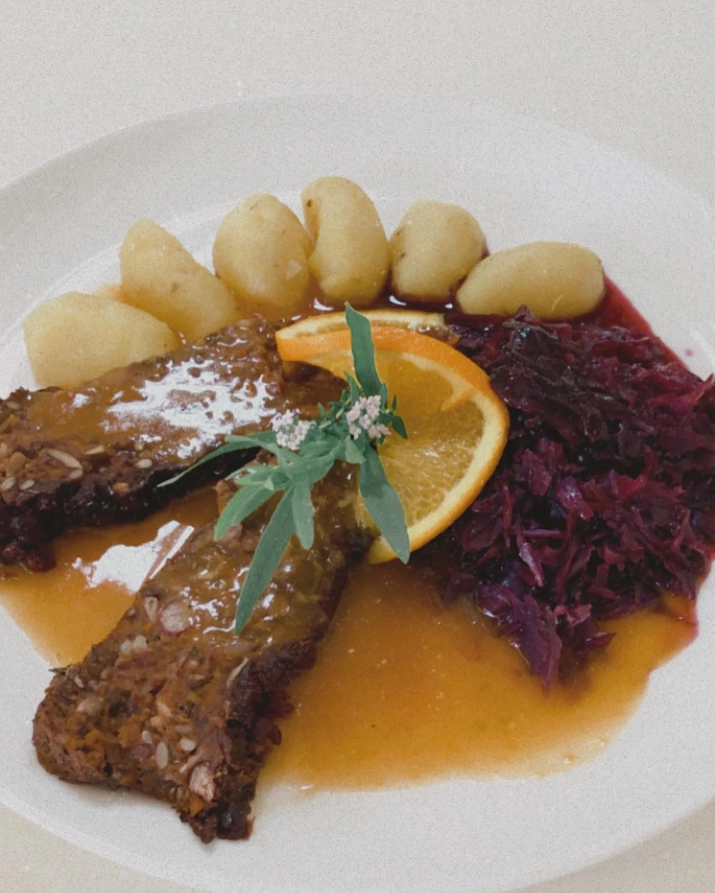 vegane Linsen-Nuss-Schnitte mit brauner Sauce, Kartoffeln, Rotkohl, Orangenscheibe, und Kräuter garnierte Speise