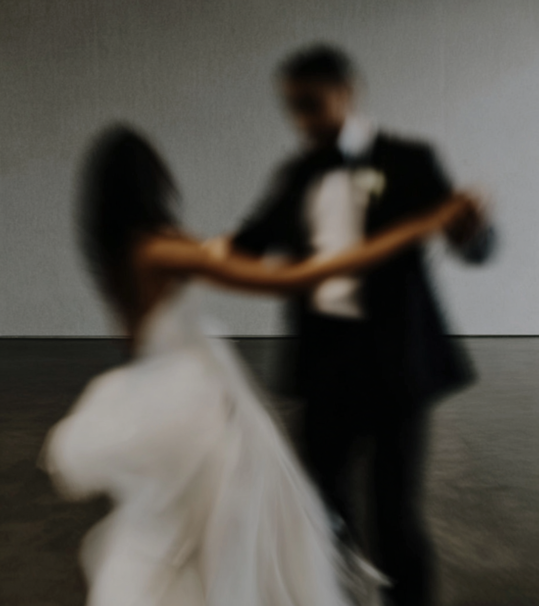Blurred photo of a couple dancing, the woman in a white dress and the man in a black suit with a bow tie.