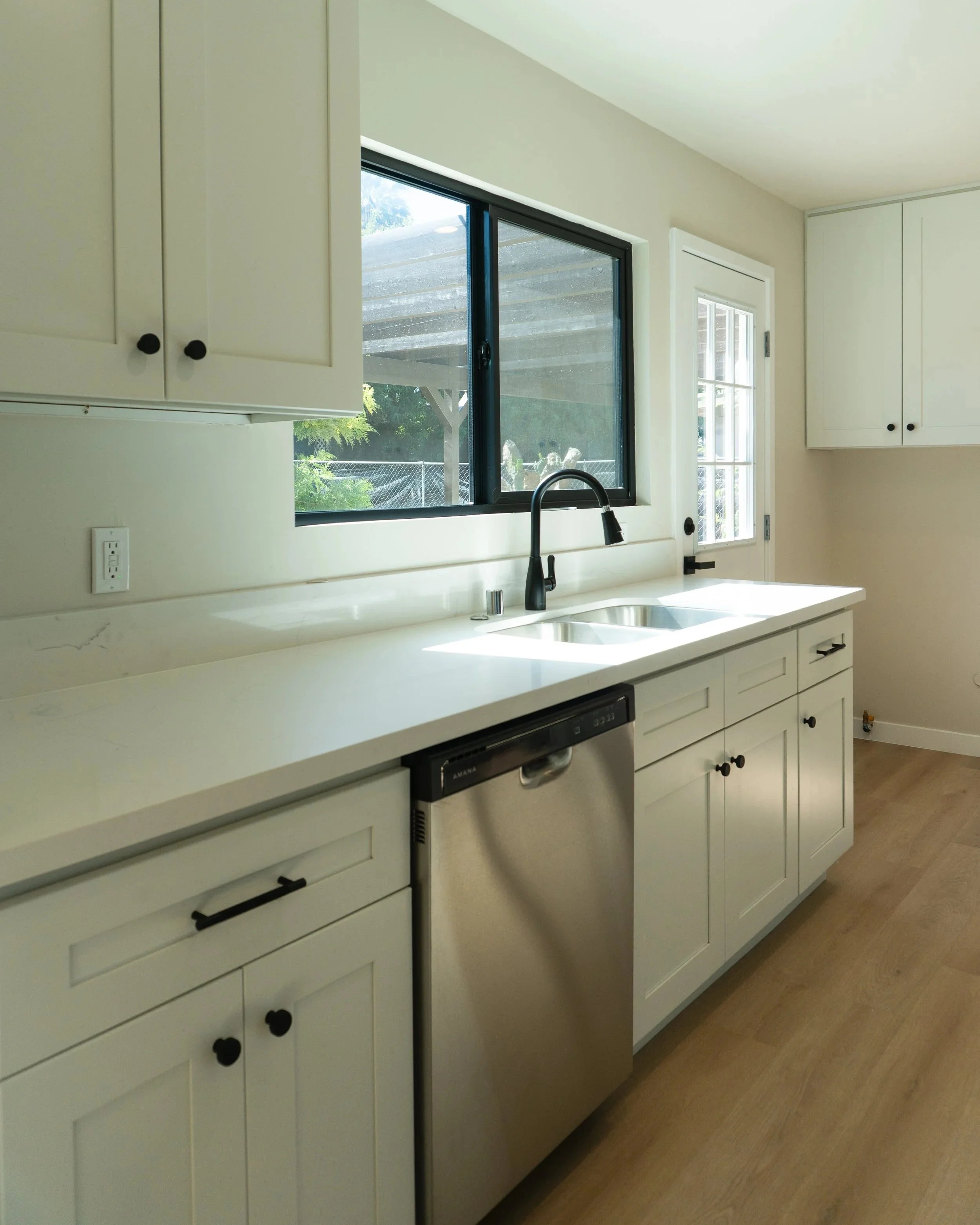 A kitchen with white cabinets, a black faucet, a stainless steel dishwasher, and a window above the sink, with natural light coming in.