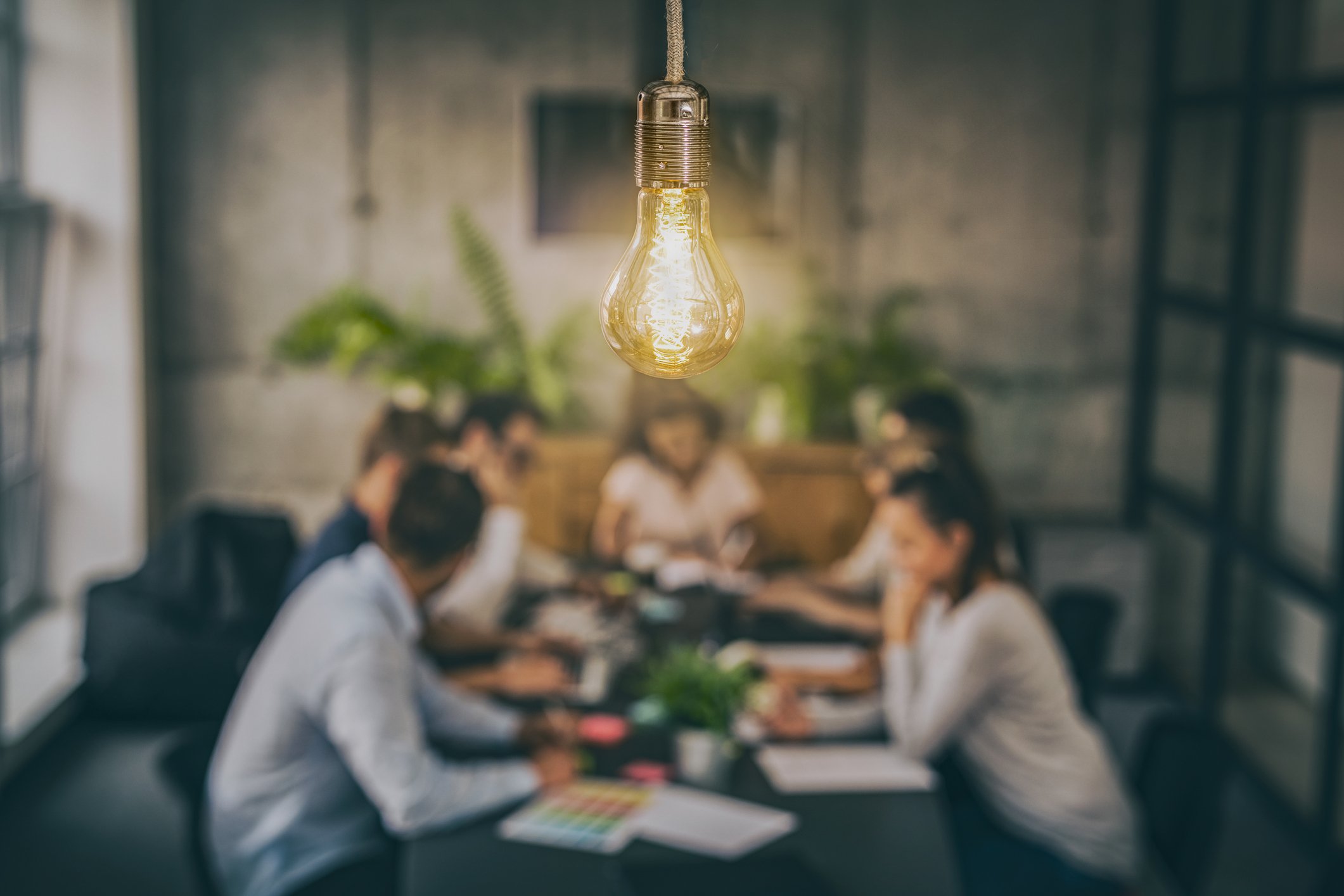 A hanging vintage-style lightbulb glowing above a group of people sitting at a table, blurred background of an indoor setting.