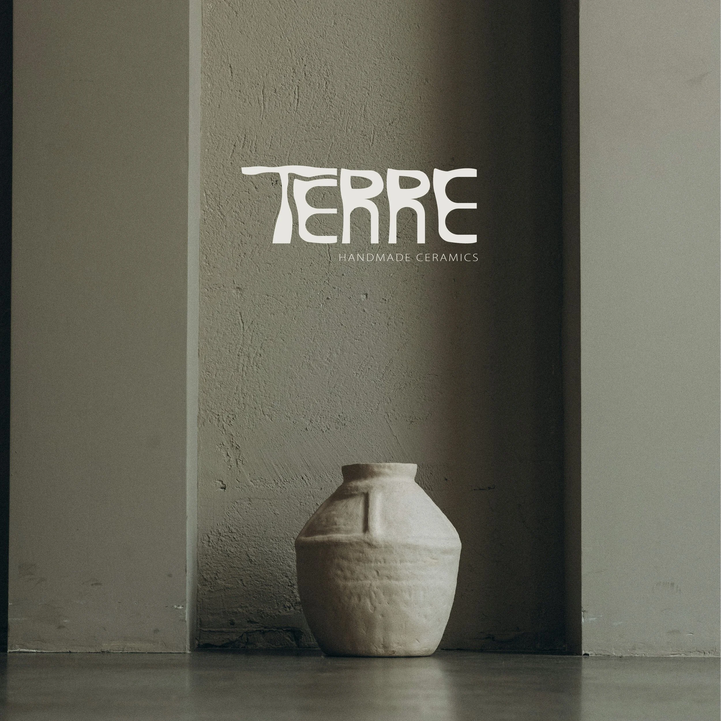 Vase en céramique beige placé au sol devant un mur gris. Logo 'TERRE' avec la mention 'handmade ceramics' en lettres blanches au-dessus du vase.