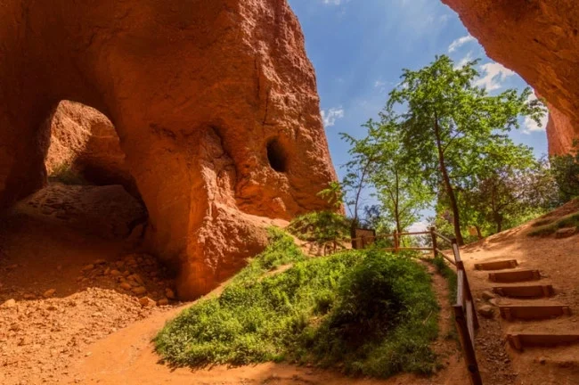 Vista de una formación rocosa natural con camino y escaleras, árboles y cielo despejado.