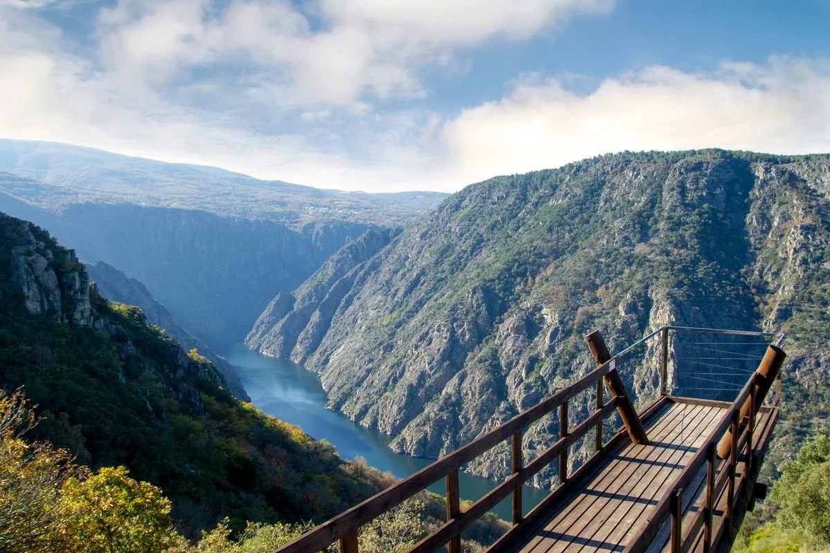 Vista de un cañón con un río en el fondo y un mirador de madera en primer plano.