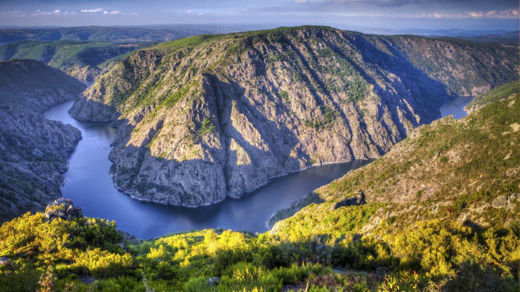 Vista panorámica de un cañón con río serpenteante, escarpadas montañas y vegetación verde en un paisaje natural.