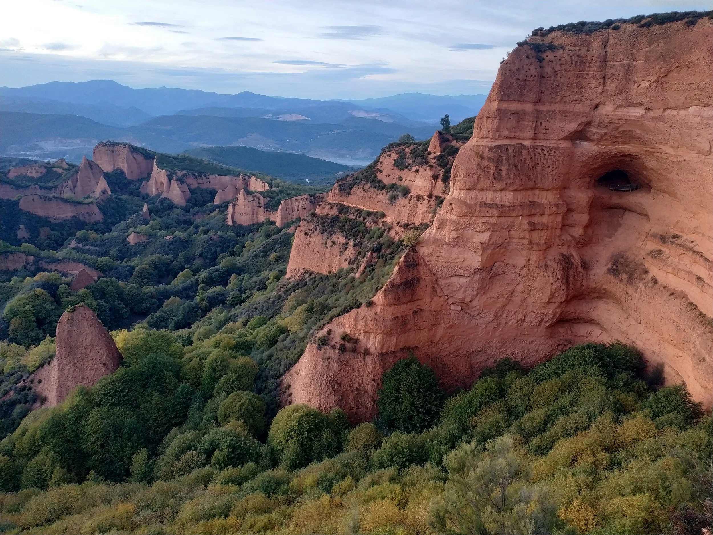 Paisaje de formaciones rocosas y montañas con vegetación verde y cielo nublado.