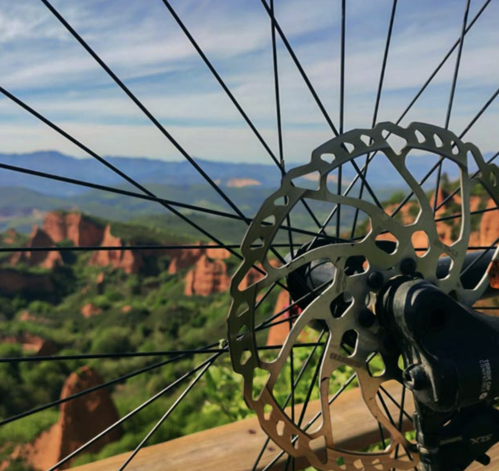 Rueda de bicicleta en primer plano con paisaje de montañas y colinas verdes en el fondo.
