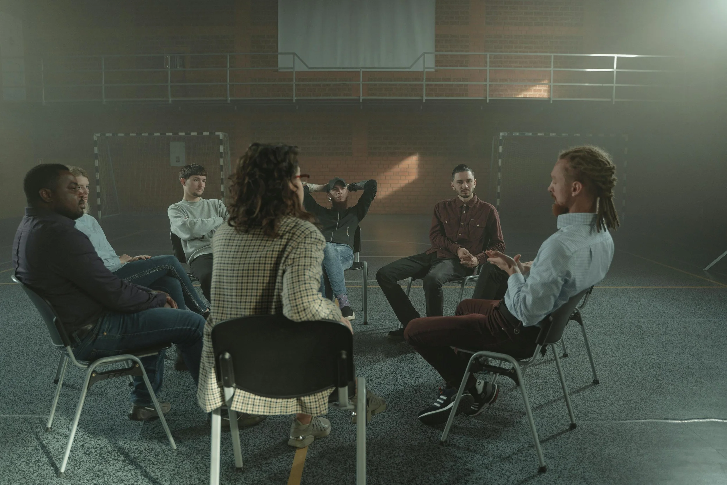 People sitting on chairs in a circle in a gynasium
