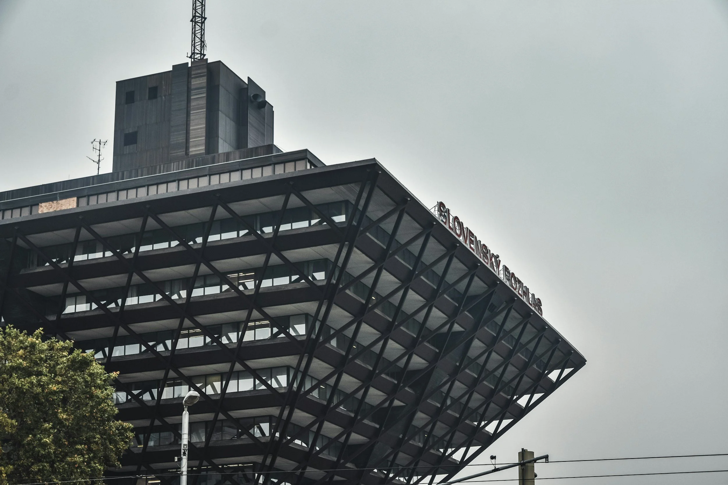 Modern building with angled steel framework, glass facade, and the sign 'Slovenské Radiotelevízie' on top, under an overcast sky.