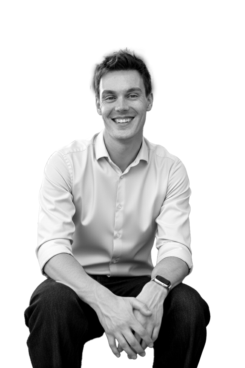 A smiling young man with short dark hair, wearing a light-colored dress shirt with the sleeves rolled up, sitting in front of a dark background with geometric shapes.