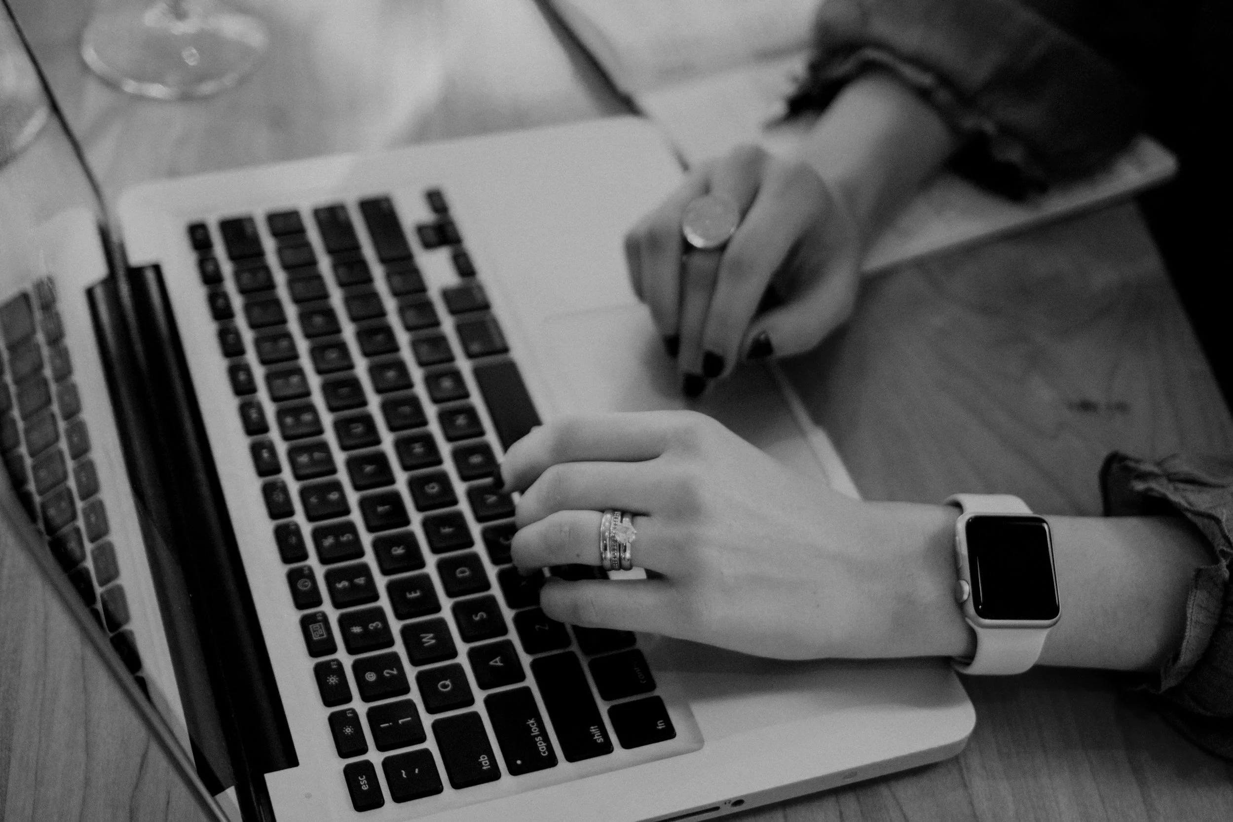 Person typing on a laptop with a smartwatch on their wrist and rings on their fingers.