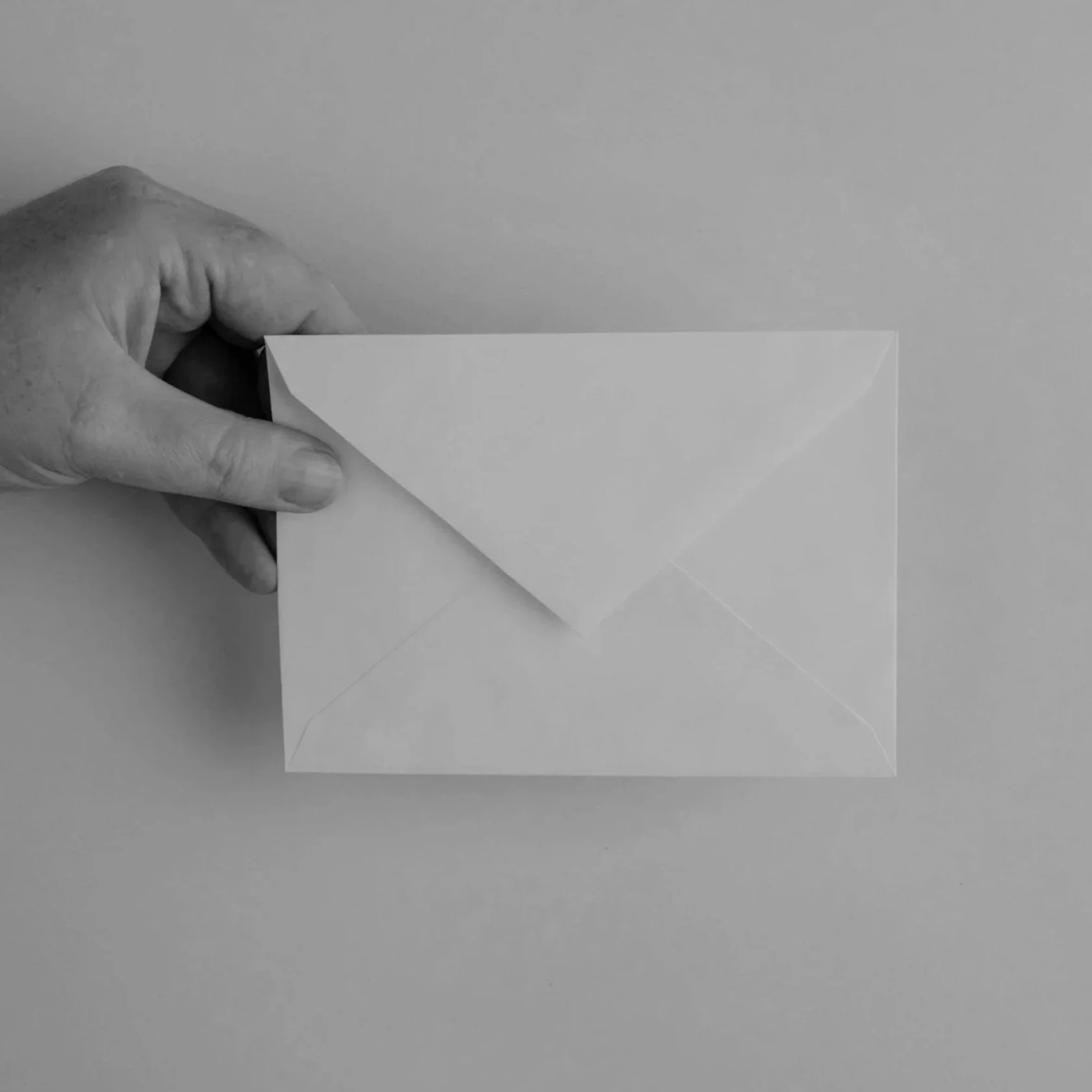 A hand holding a sealed envelope on a plain surface.