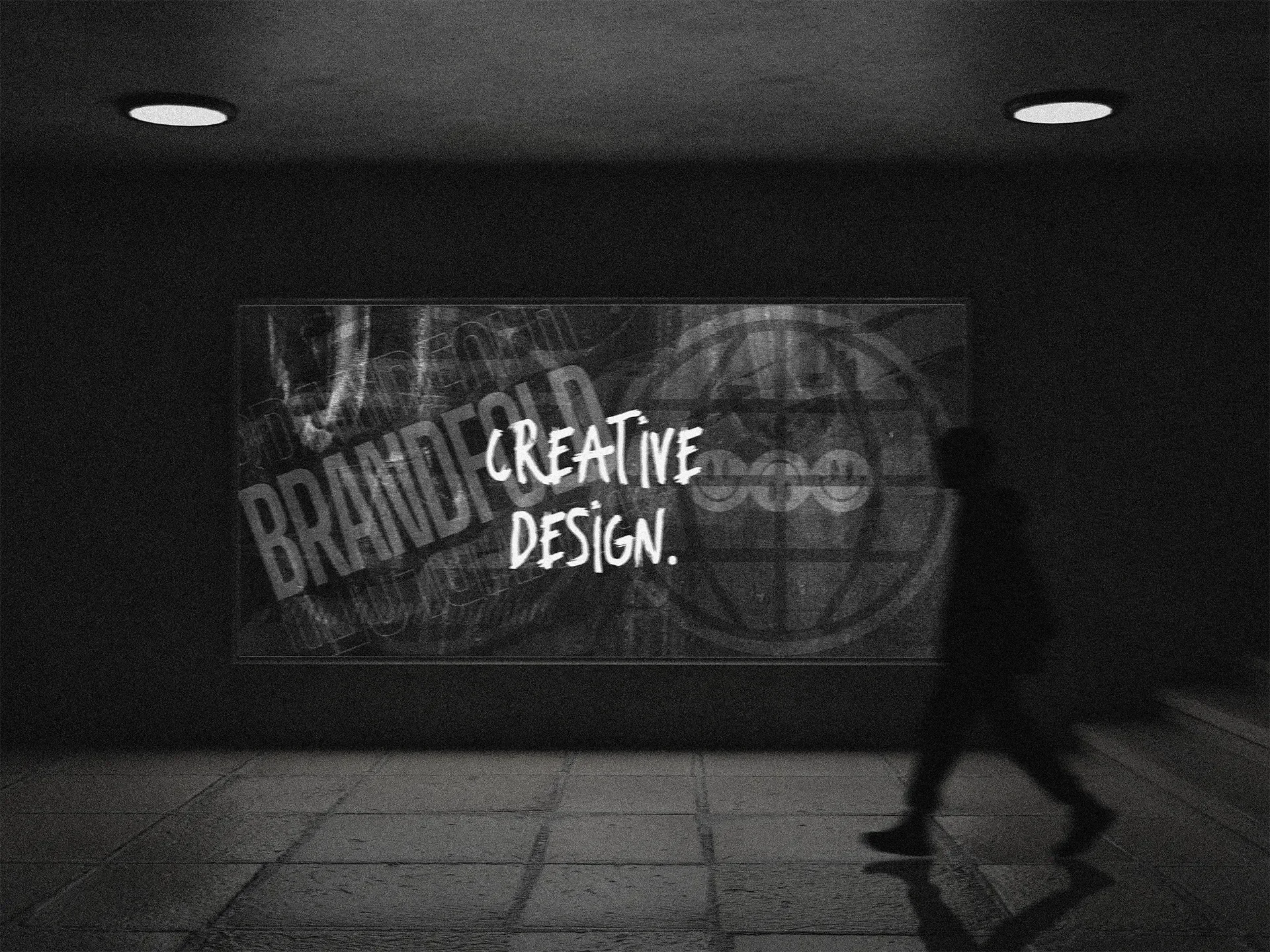 Een zwarte en witte foto van een persoon die op een vloer loopt in een overdekte ruimte met een verlichte muur waarop een creatieve reclame staat met de woorden 'CREATIVE DESIGN.'
