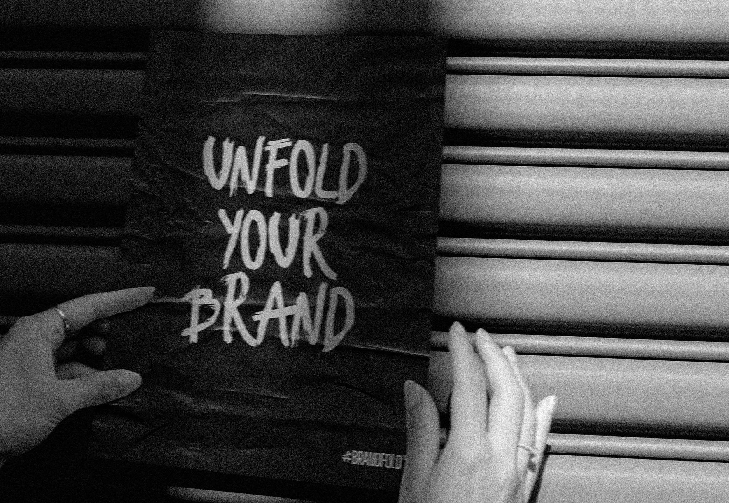 Een vrouw die een affiche vasthoudt met daarop het opschrift 'Unfold your brand' en het logo van Brandfold erop.
