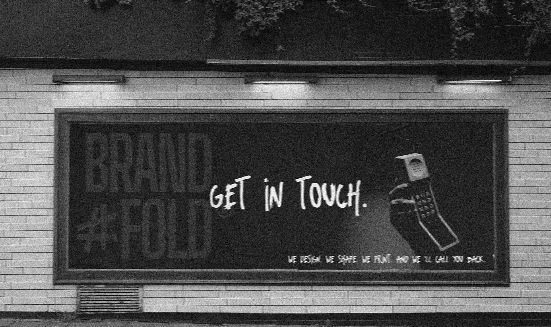 Een grote reclameposter op een muur met de tekst 'GET IN TOUCH' en een afbeelding van een oude mobiele telefoon. De achtergrond bevat de woorden 'BRAND' en '#FOLD' en een korte tekst onderaan.