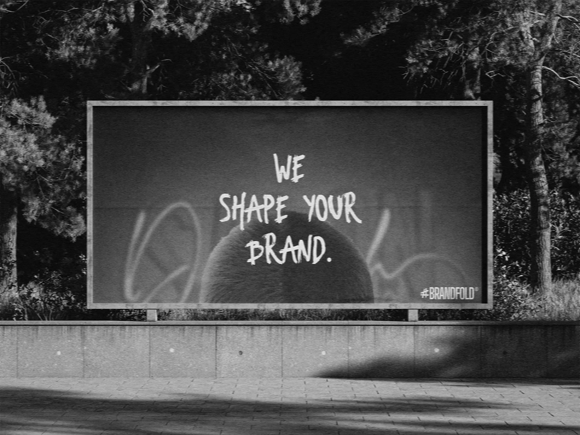Een billboard met de tekst 'We shape your brand' en een afbeelding van een hoofd met oortelefoons, tussen bomen.