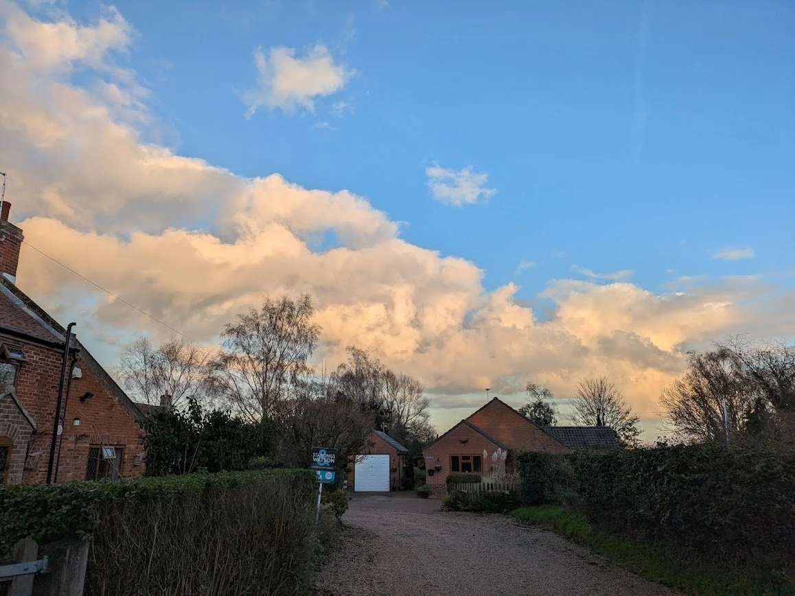 Traditional English village cottages under a golden sunset sky, inspiration for Lucy Emblem’s cozy mystery setting