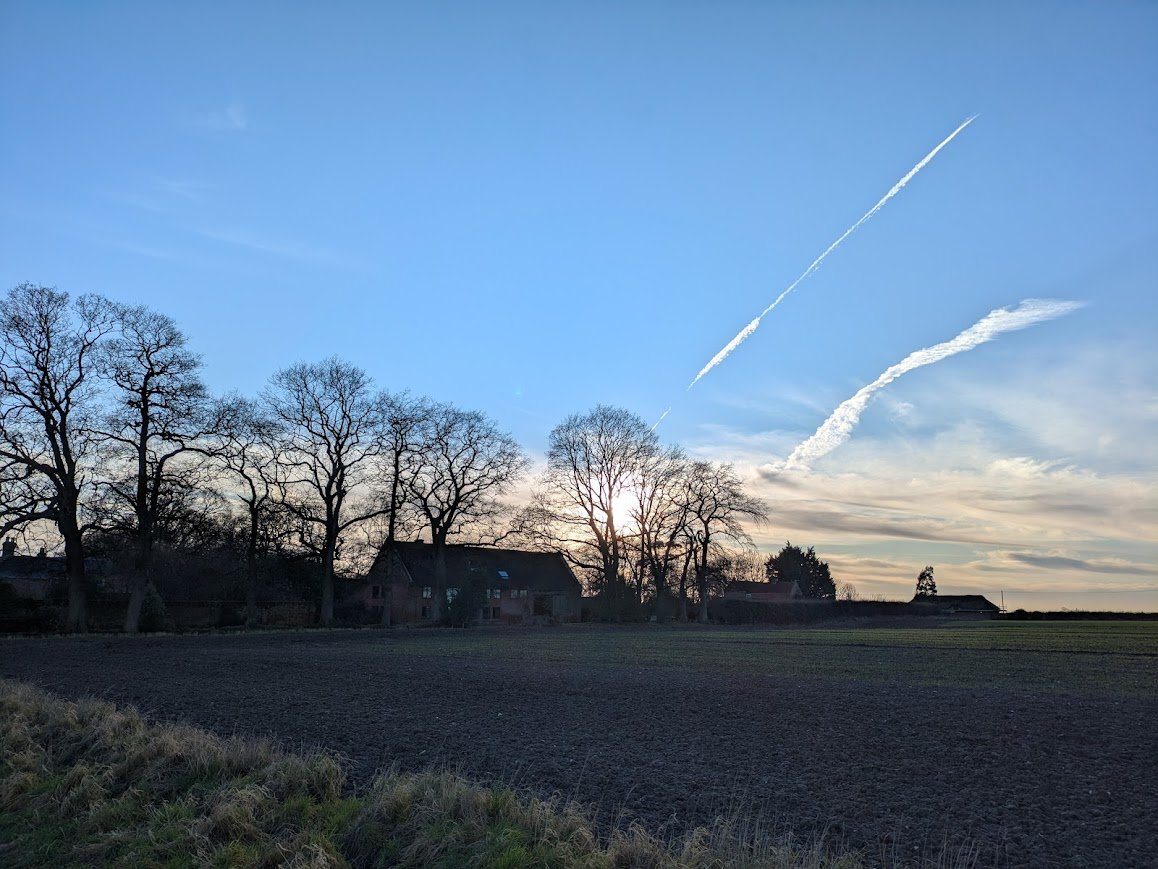 Rural English farmhouse and winter fields beneath a wide evening sky, reflecting the countryside setting of Lucy Emblem’s cozy mysteries