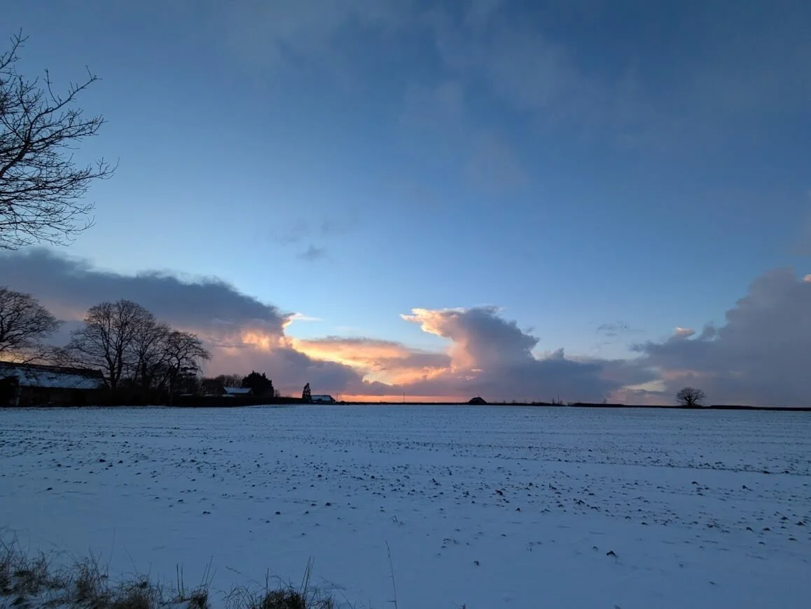 Snow-covered English farmland at sunset, part of the rural setting in Lucy Emblem’s cozy mystery novels