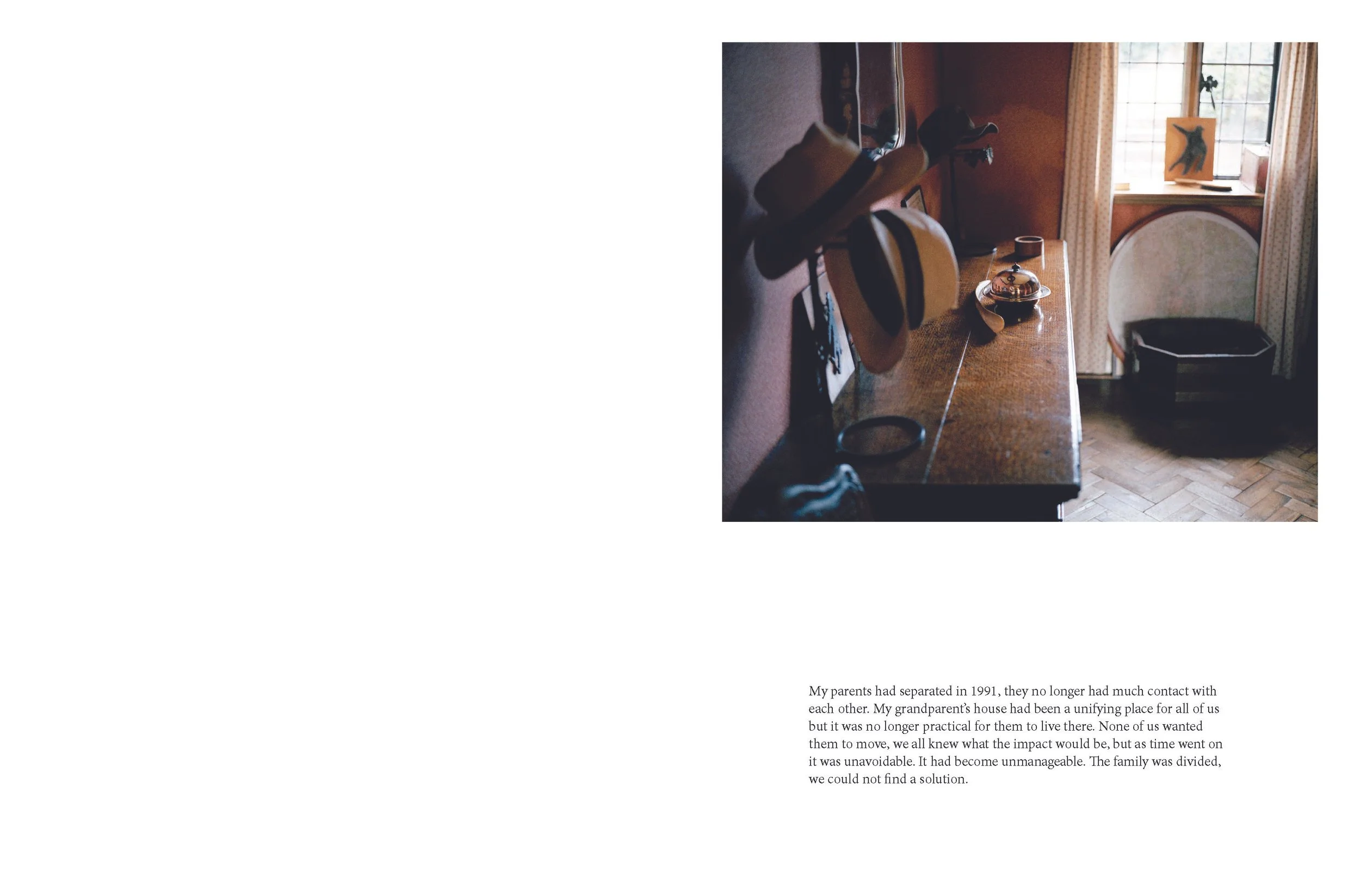 A photograph of a corner of a room with sunlight coming through a window. There is a wooden table with objects on it, including a hat, a bottle, and some other small items. A window with curtains, a framed artwork, and a black tray or box are visible