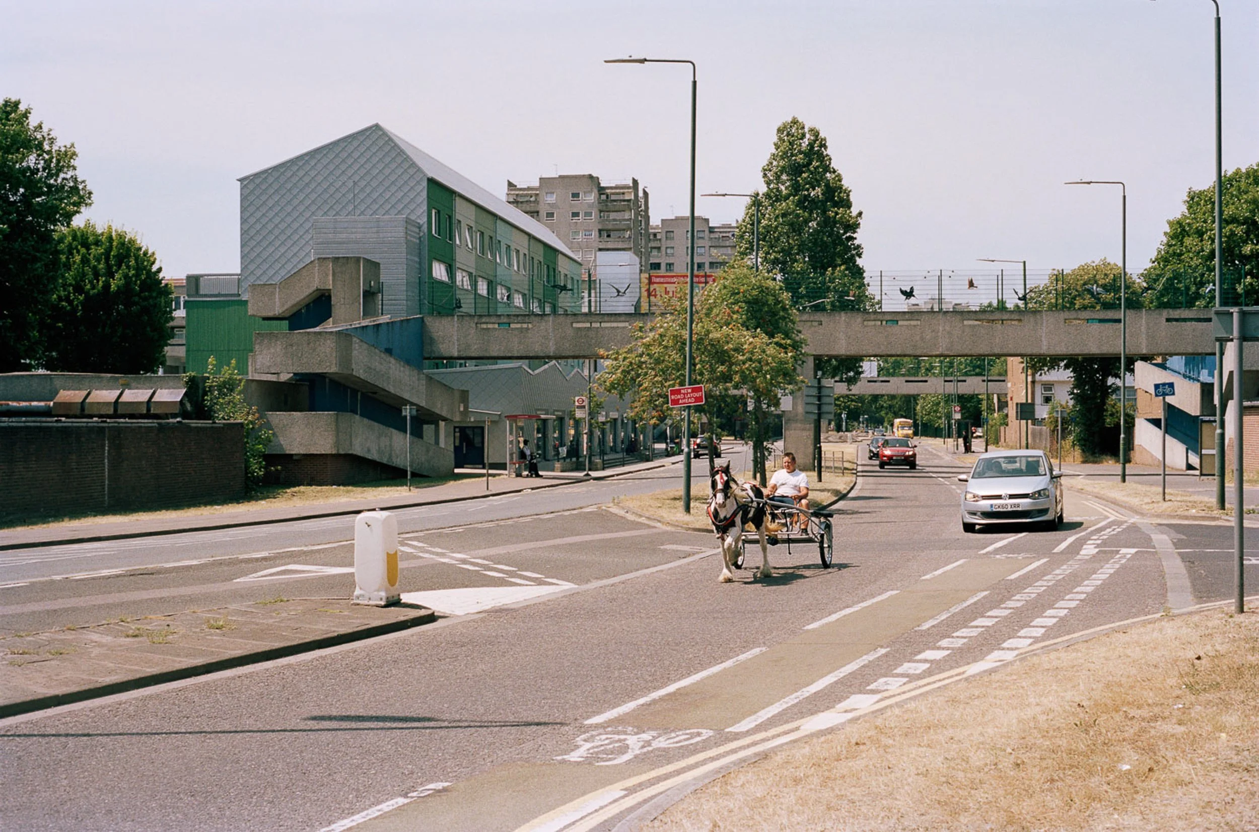 A city street with a horse-drawn cart, pedestrians, cars, modern buildings, and a pedestrian bridge.