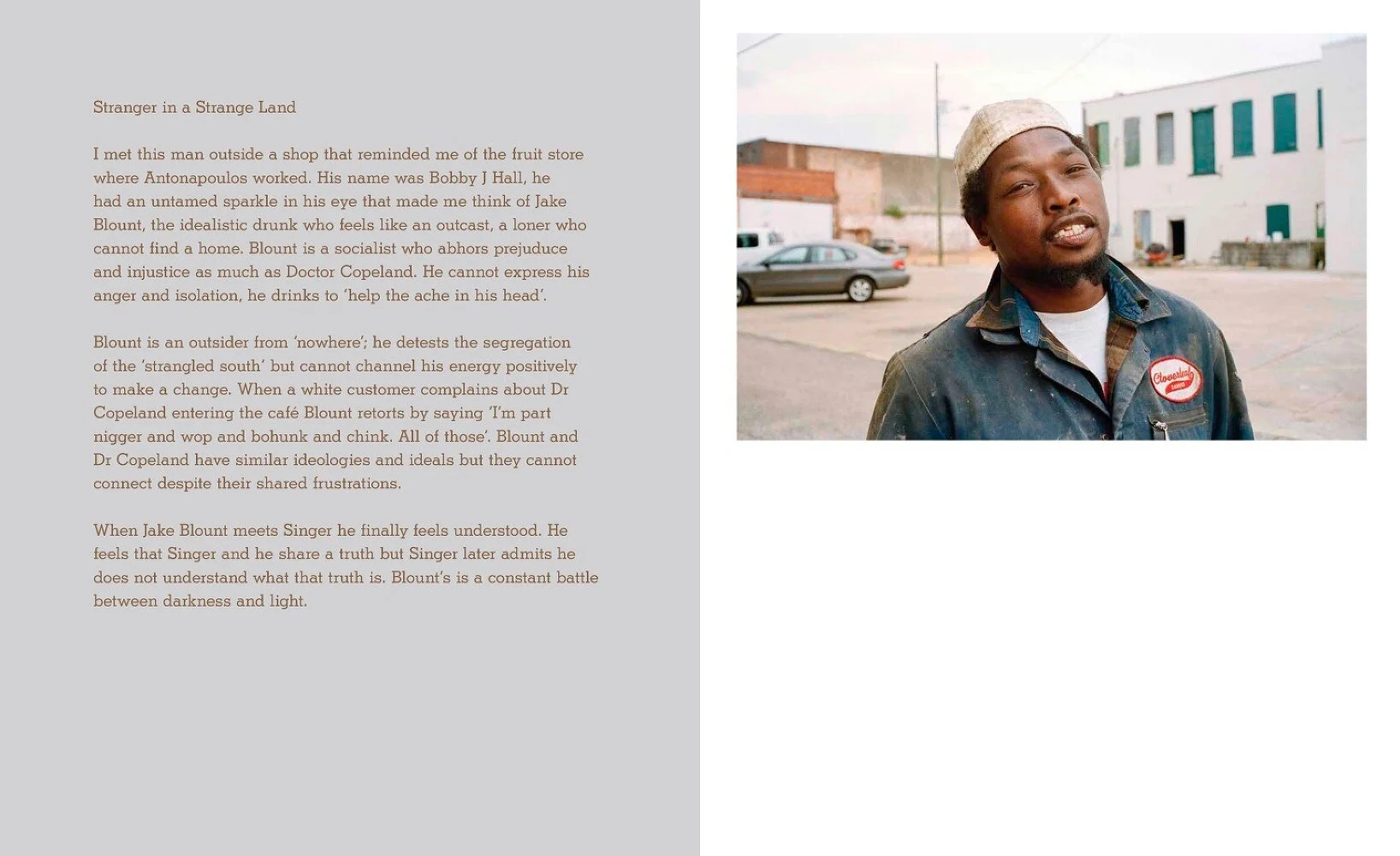 A young Black man wearing a cap and a work uniform with a name tag, standing outdoors on a street with parked cars and buildings in the background.